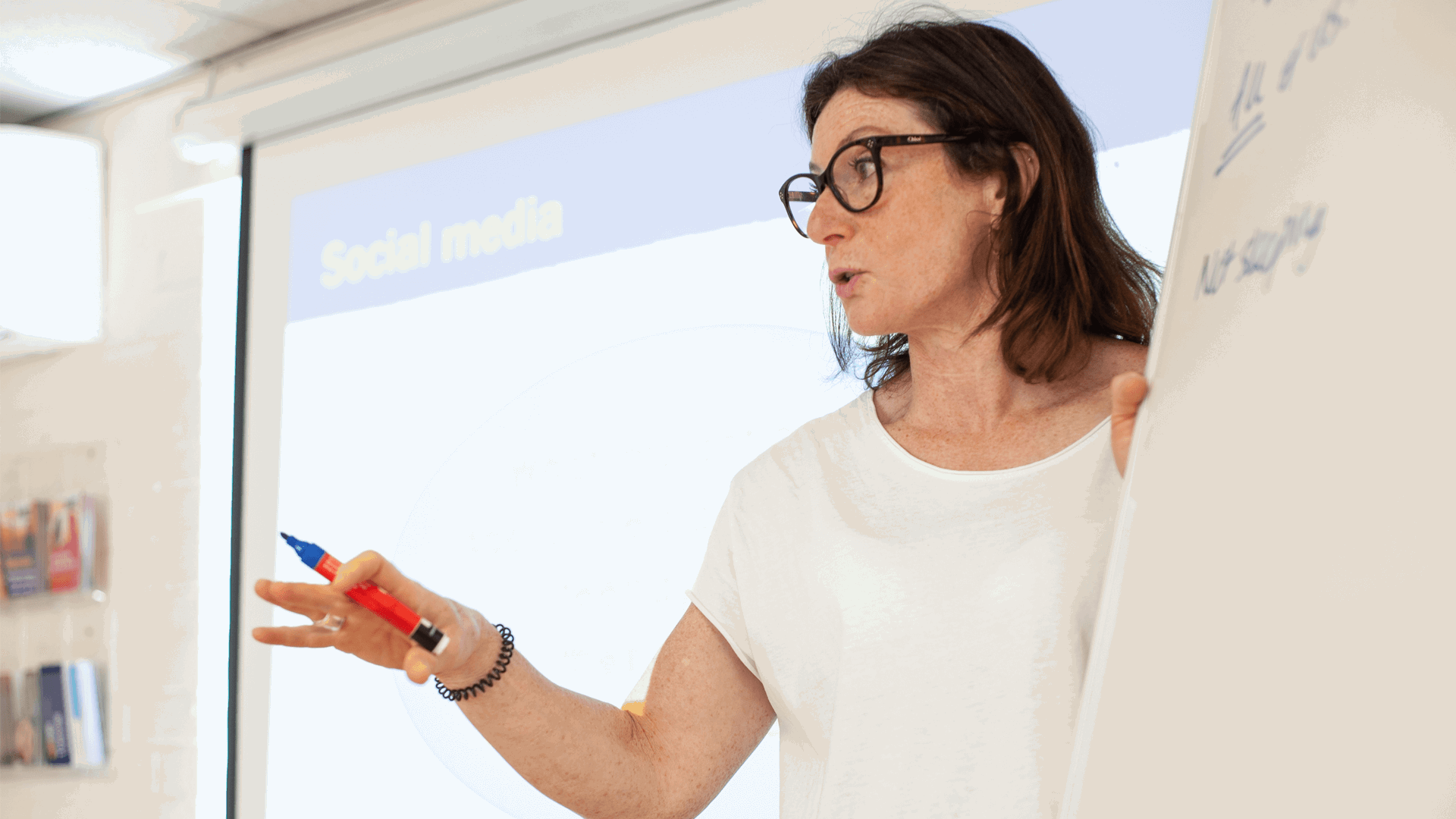 a teacher wearing eyeglasses and holding a marker is doing a lecture in classroom