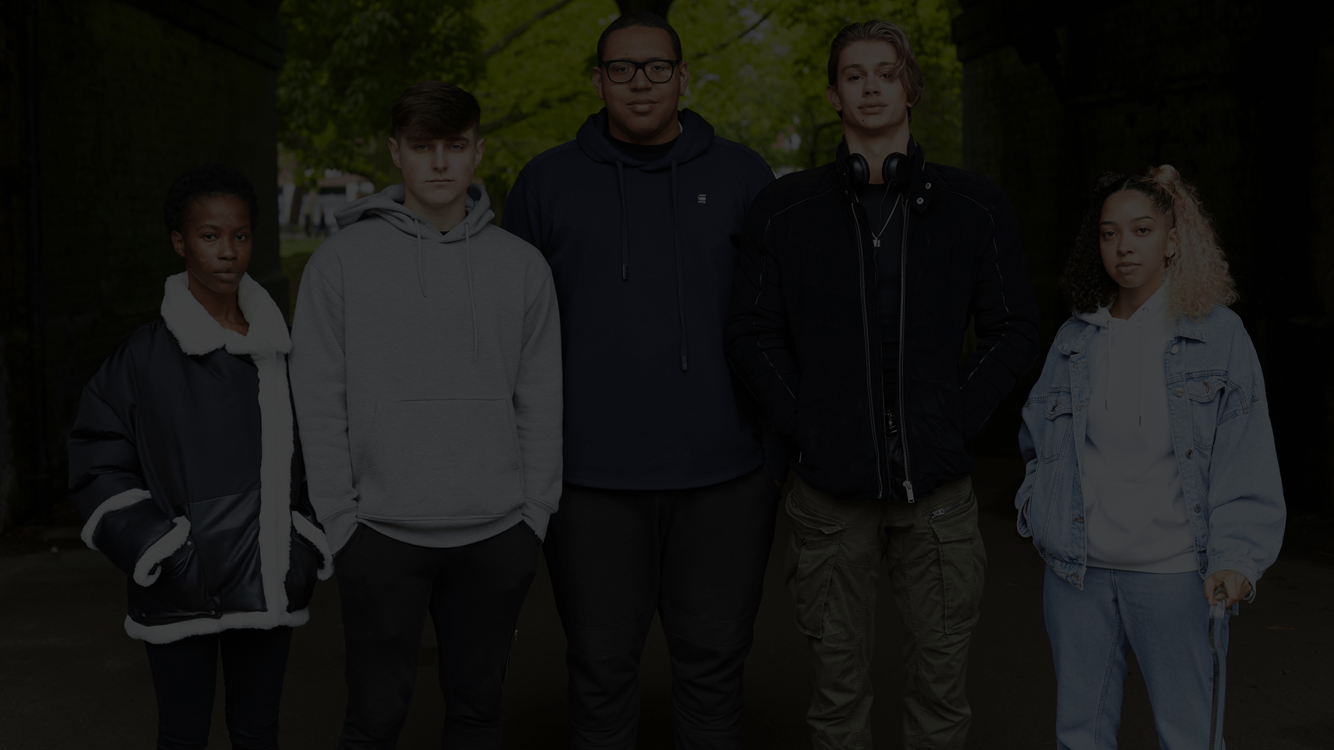 Five young people standing and looking at the camera with trees in the background.