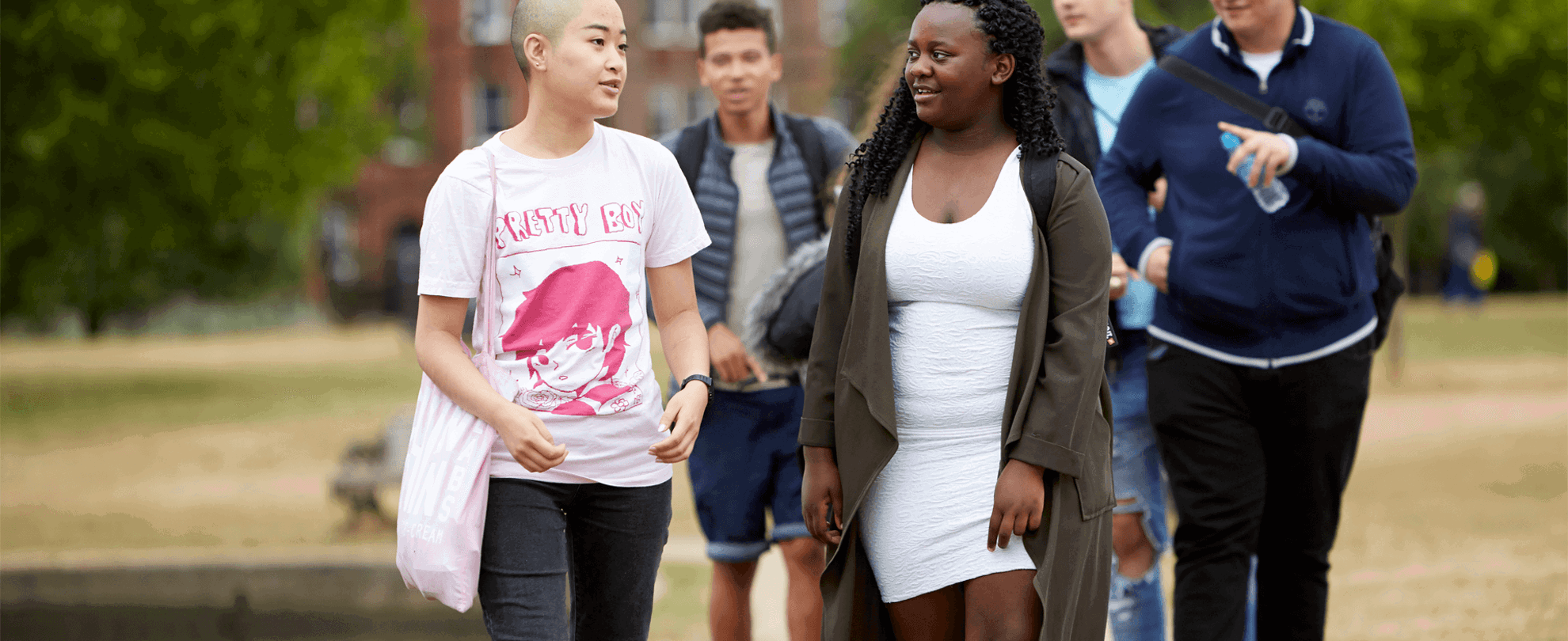 A group of five young people walking together along a path in the park. Two girls are walking ahead and talking, while three boys walk behind them.