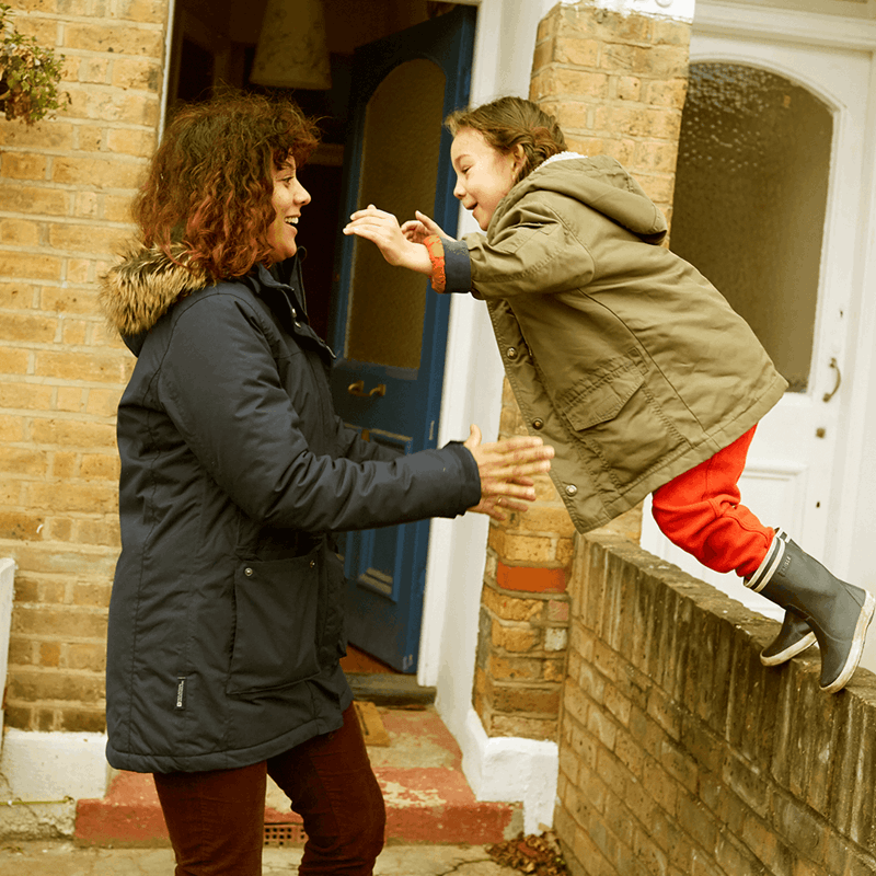A child jumping off a wall and her mum is ready to catch her.