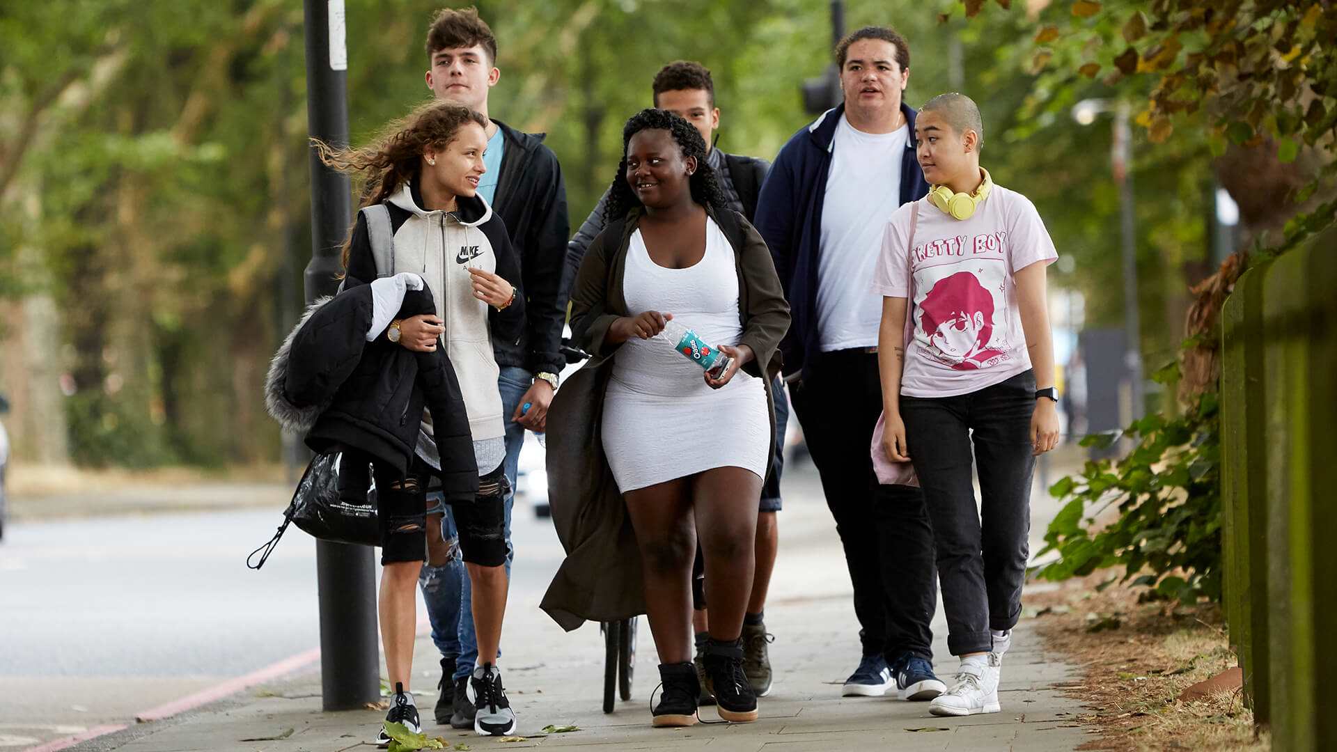 Six young people chatting as they walk through a park together.