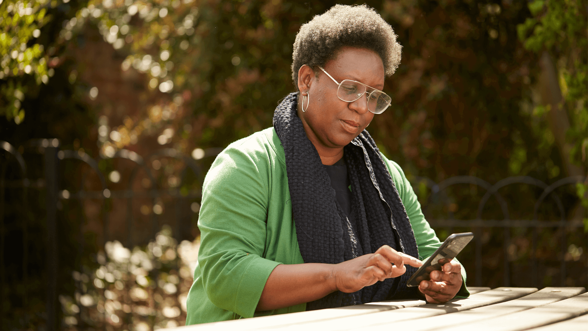 A lady typing on her phone while sitting at a picnic table