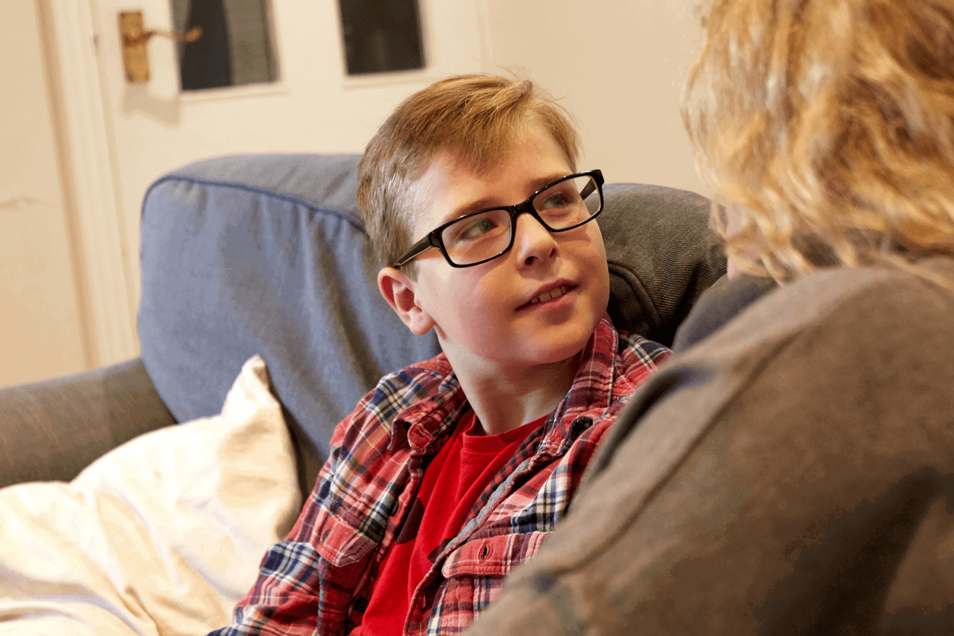 A young boy sitting on a sofa looking up at his mum 