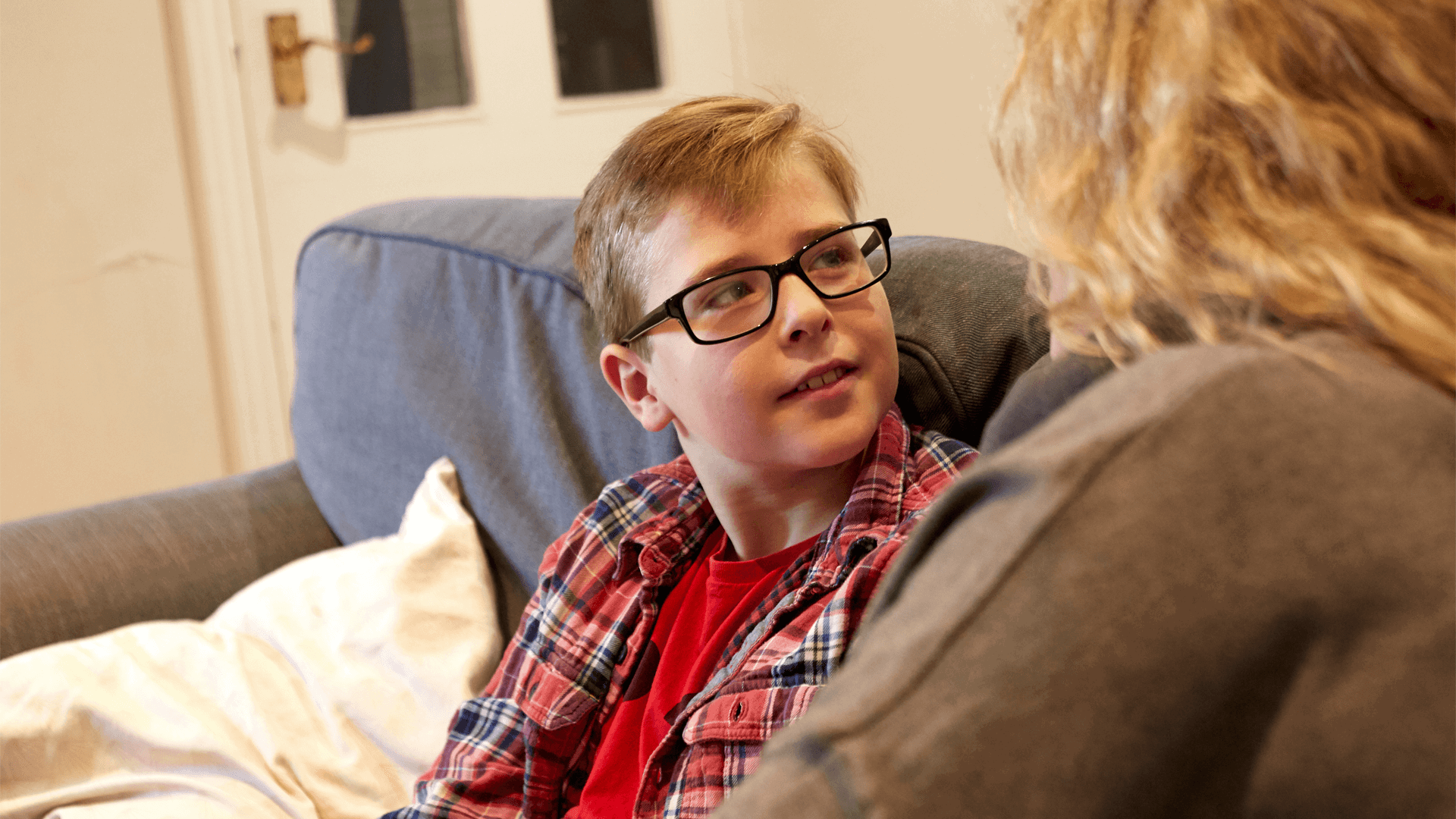 A young boy sitting on a sofa looking up at his mum 