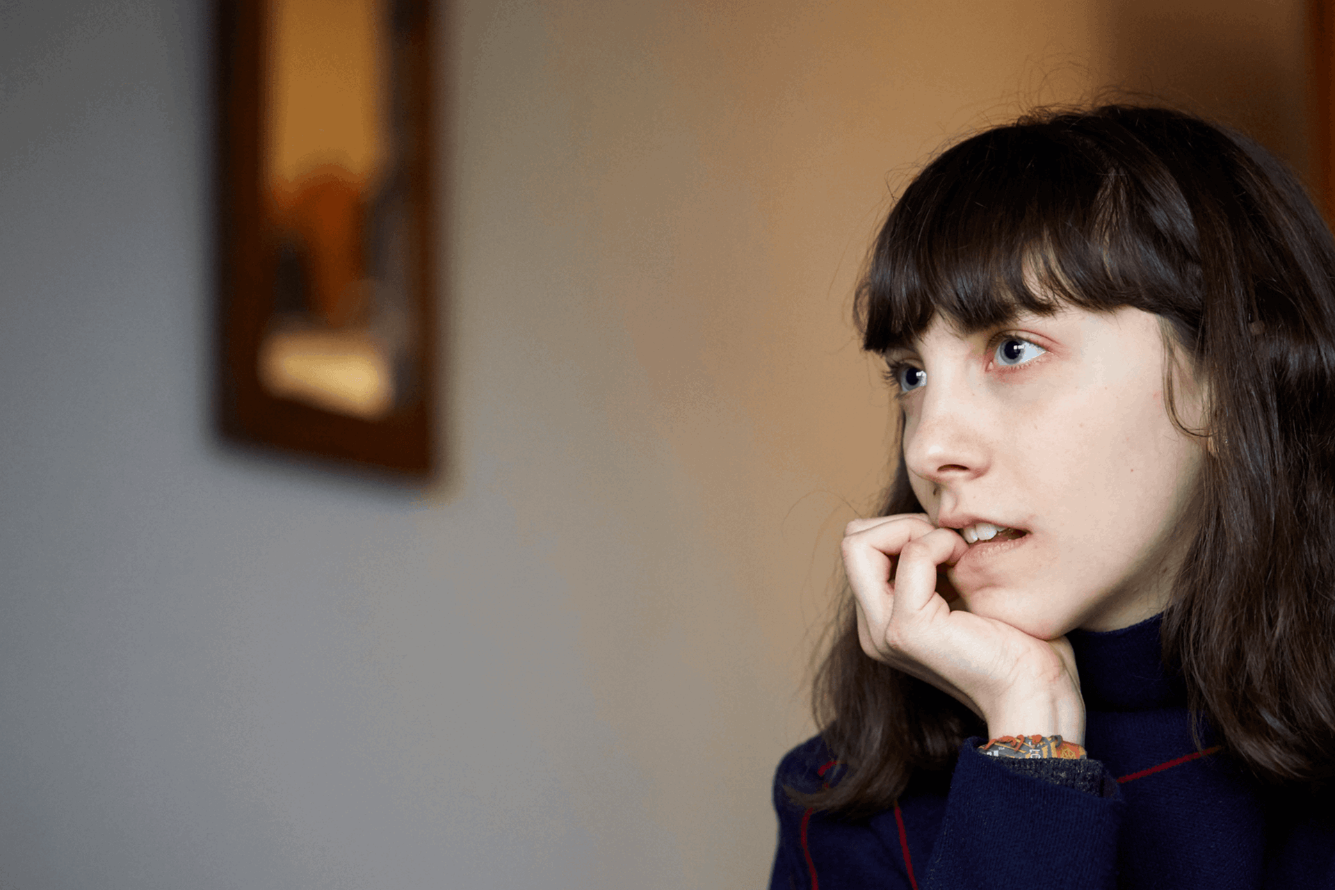 close up of a girl with fringe and wearing black jumper looking away and biting her fingers