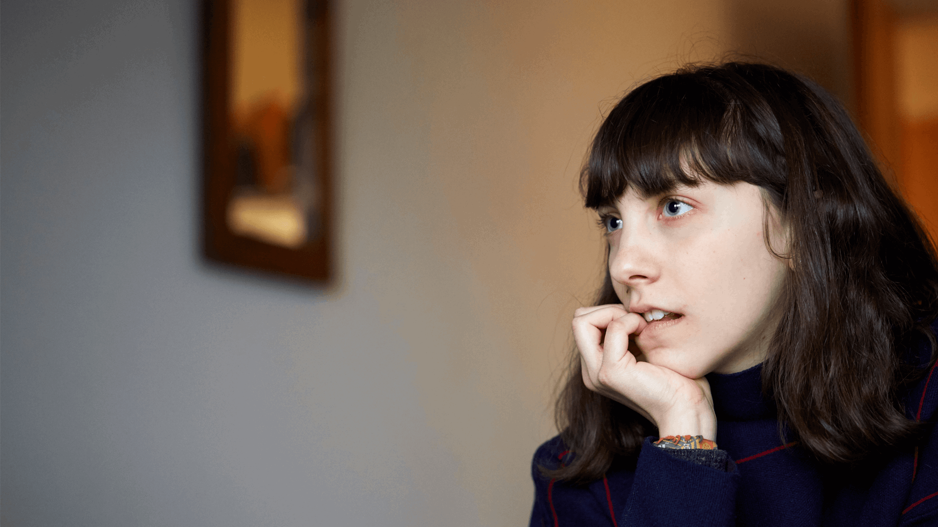 close up of a girl with fringe and wearing black jumper looking away and biting her fingers