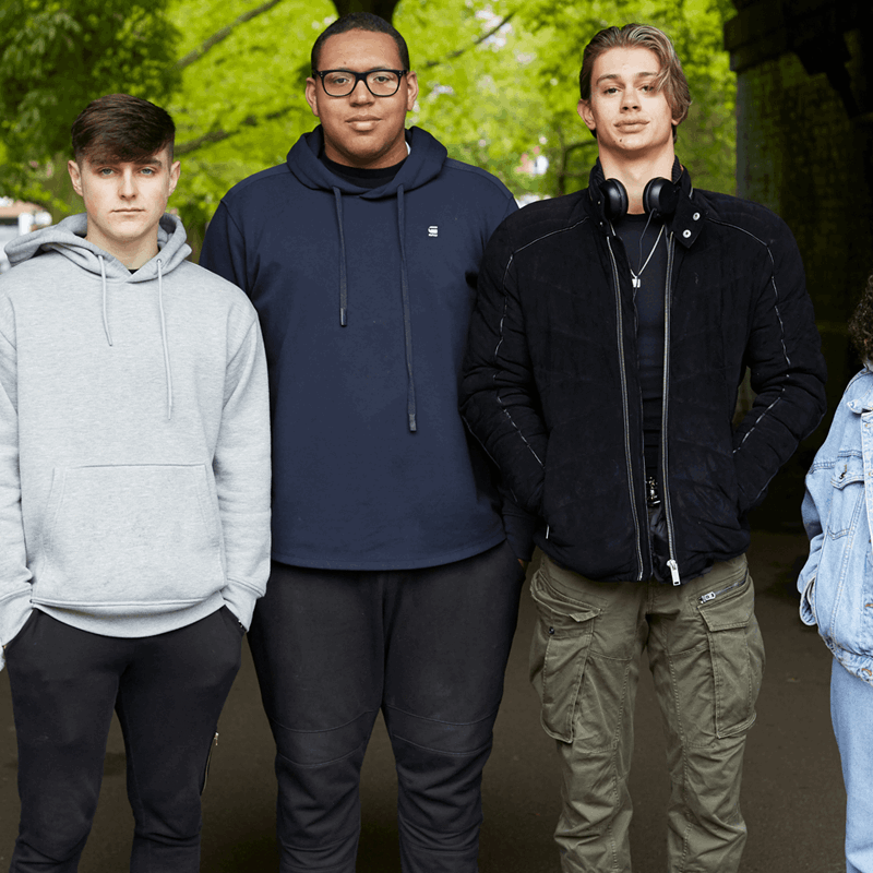 Five young people standing and looking at the camera with trees in the background.