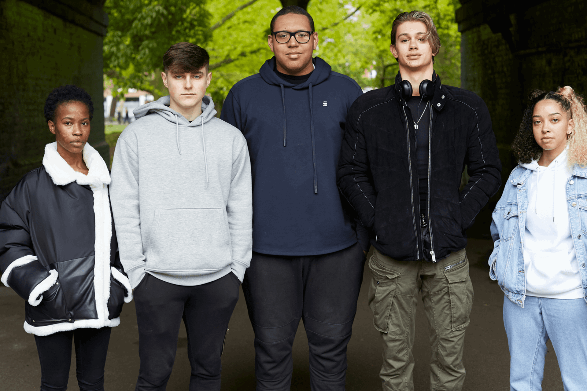 Five young people standing and looking at the camera with trees in the background.