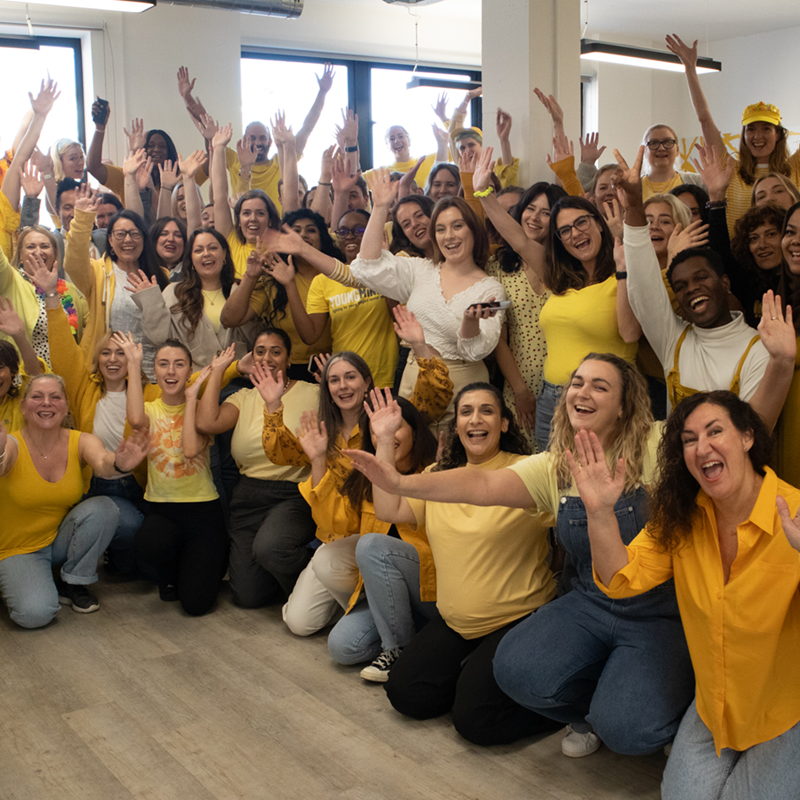 YoungMinds staff all wearing yellow for #HelloYellow 2023, posing with their hands in the air.