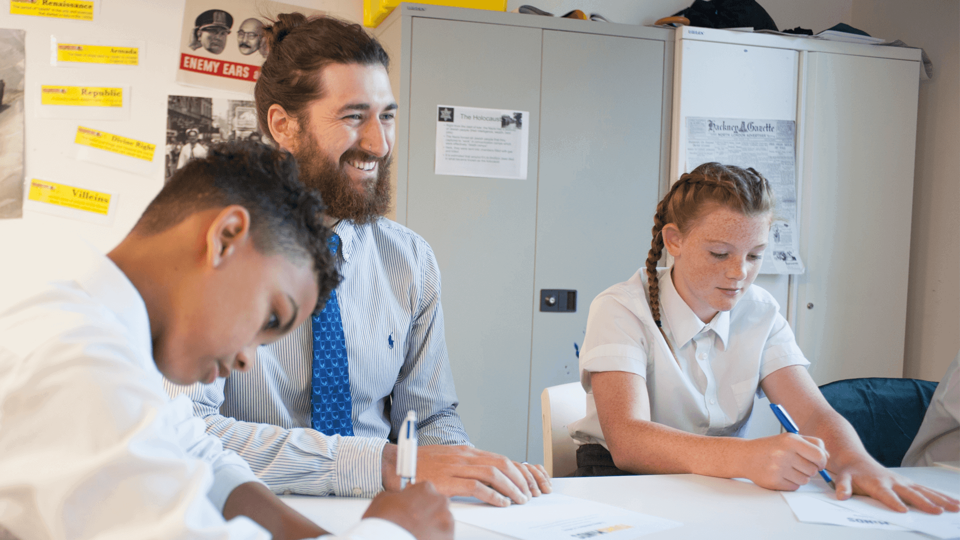 A male teacher laughing with students in a classroom
