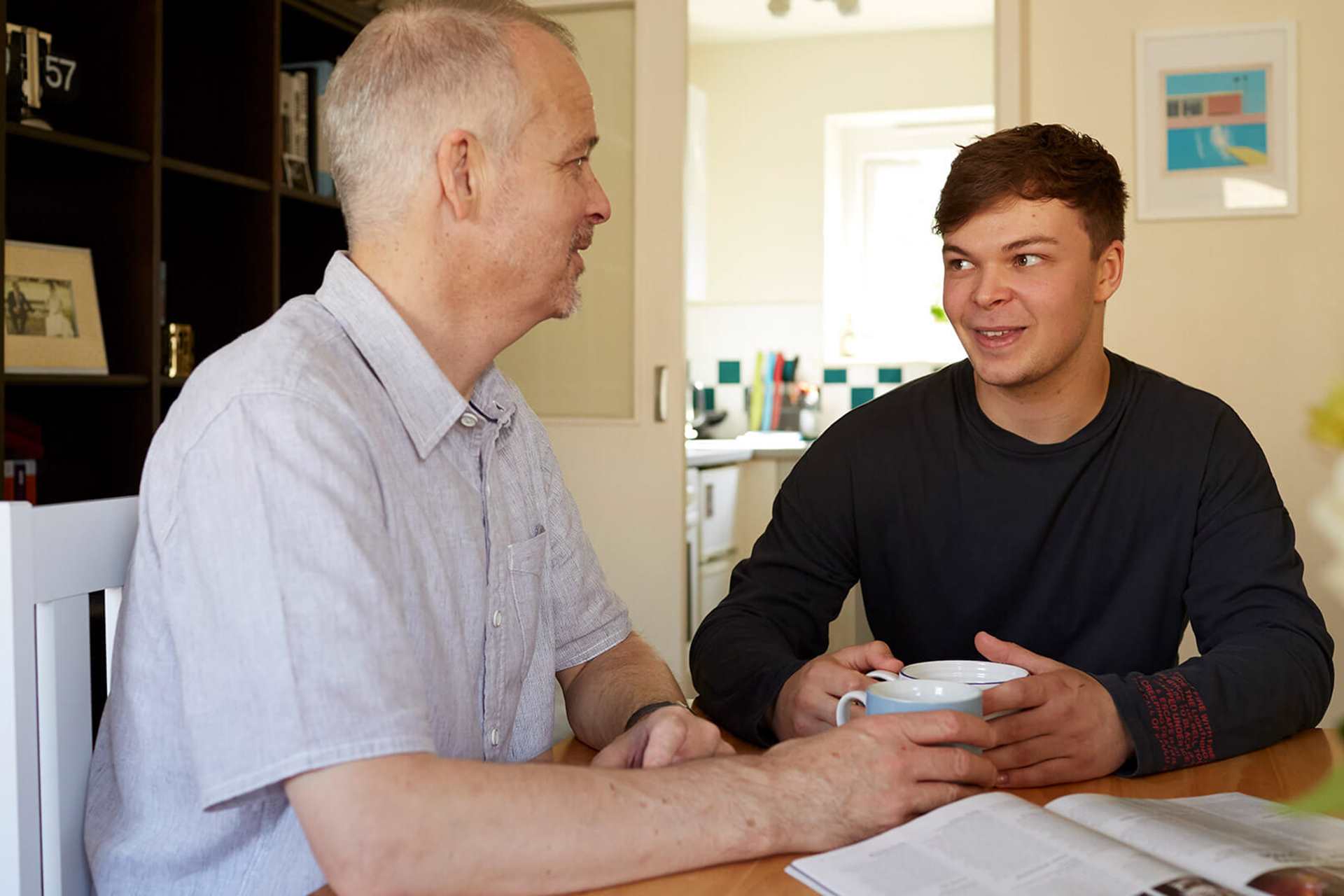 A father and son sitting at a table smiling with hot drinks