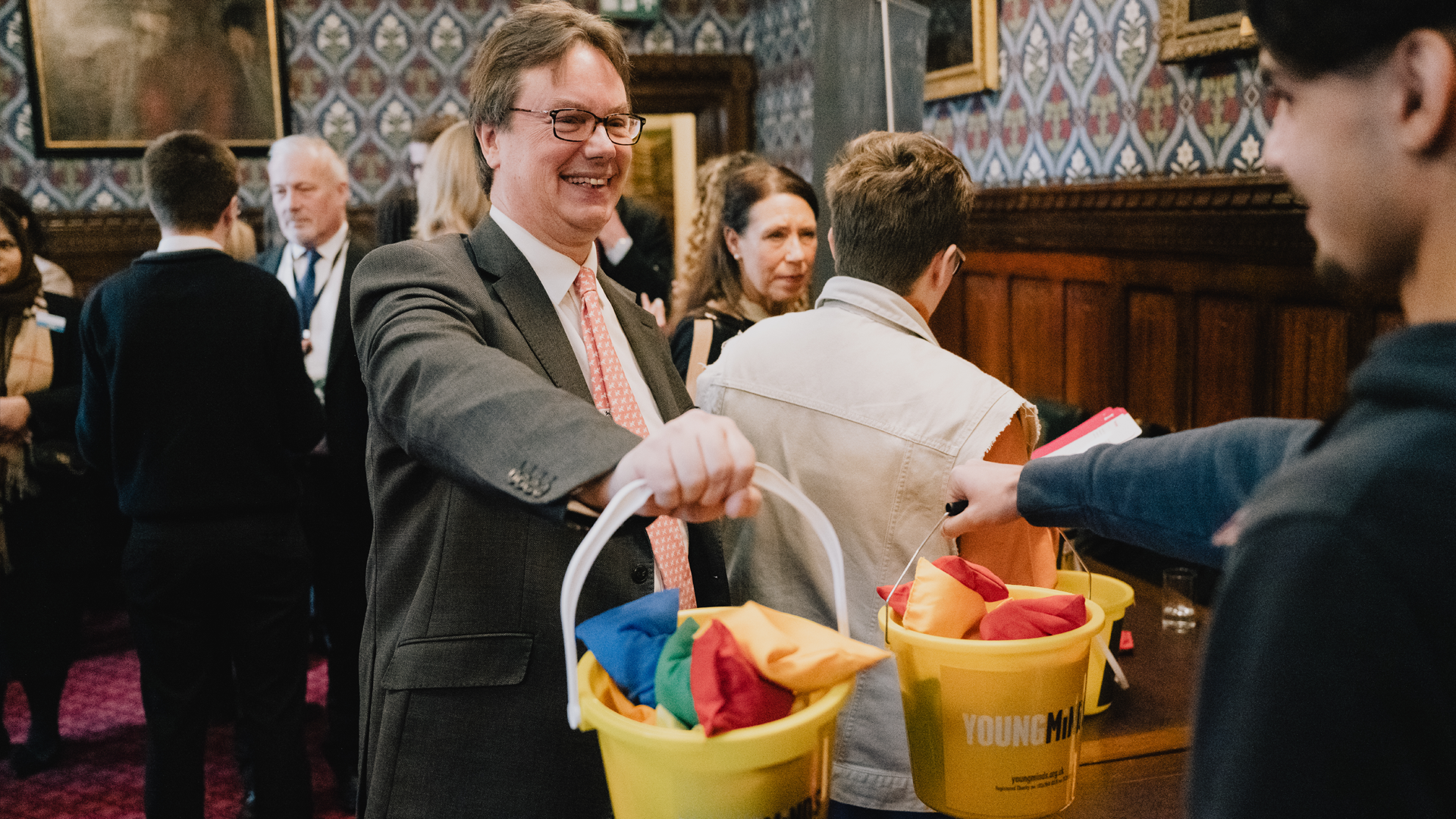 An MP and an Activist holding two heavy buckets full of bean bags, their arms outstretched.