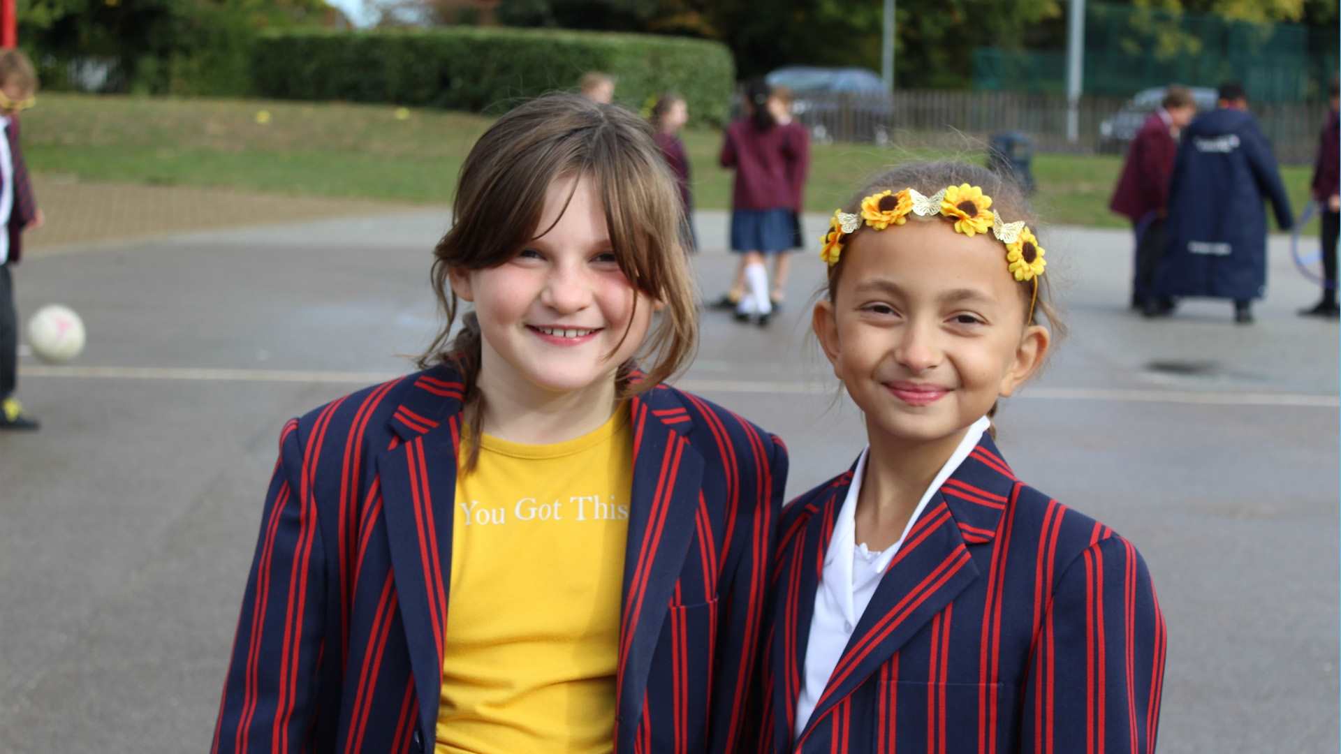 Two children standing in the playground, smiling and wearing yellow.