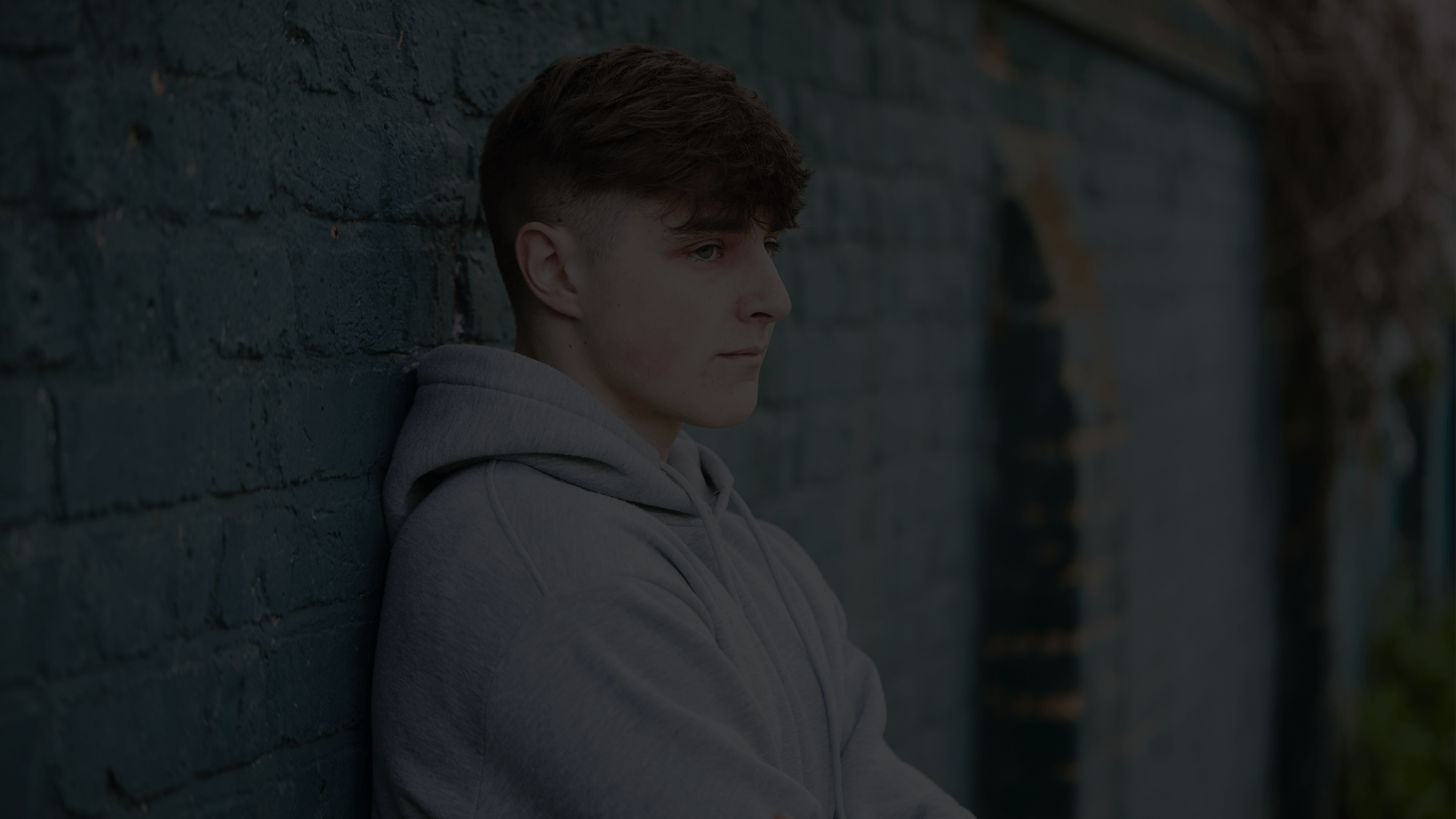 A young person standing with their back against a brick wall.