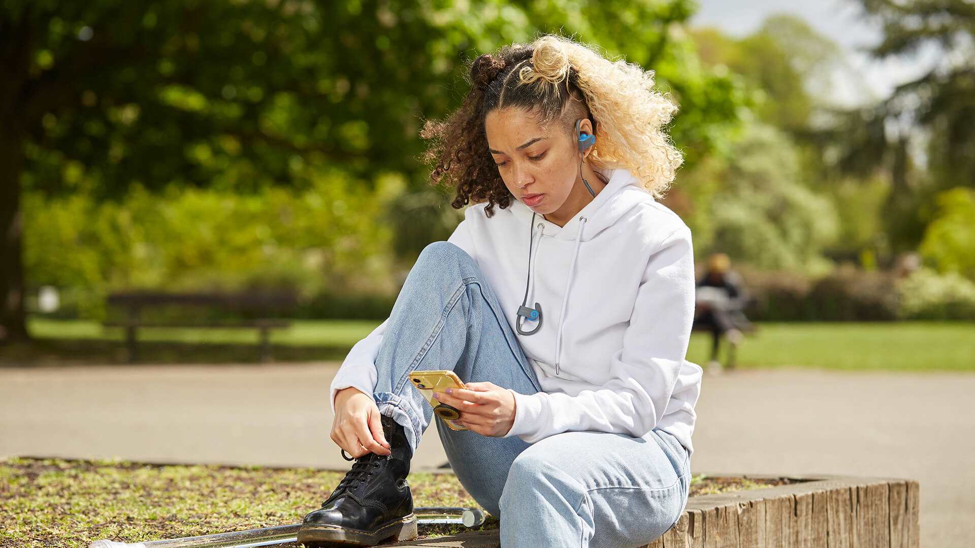 wide-shot-of-a-girl-with-headphones-and-looking-at-her-phones-while-sitting-in-the-park