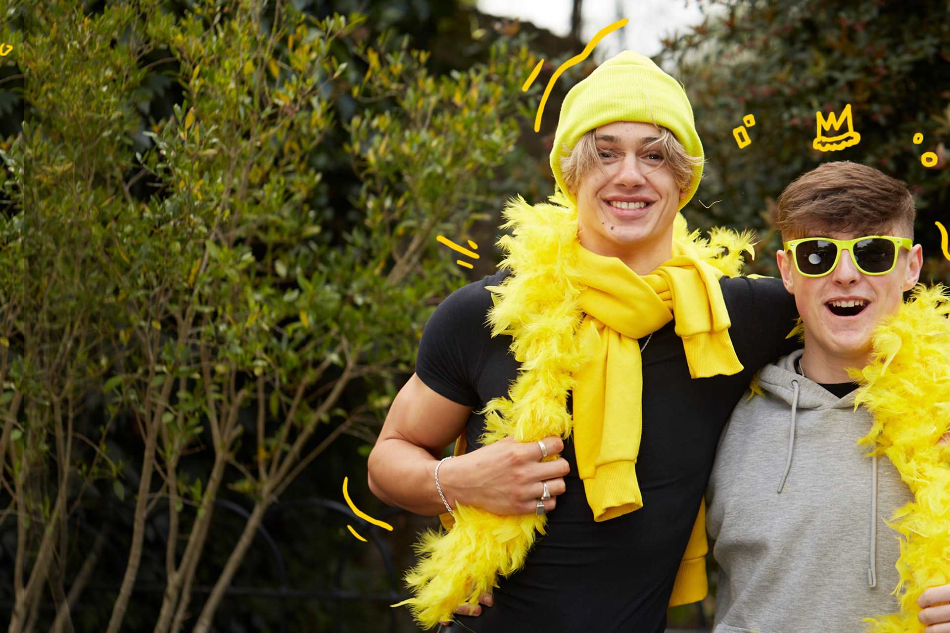 Two young people with their arms around each other. They are wearing a yellow feather boa, yellow hat and yellow sunglasses.