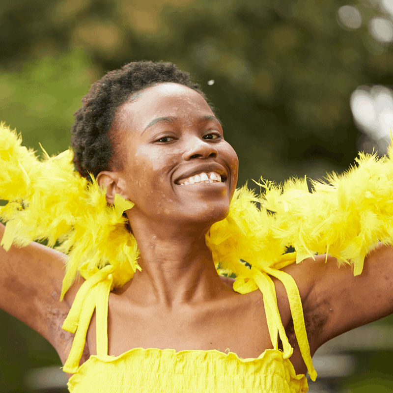 medium shot of a fundraising ambassador wearing yellow dress and yellow feather scarf smiling at the camera