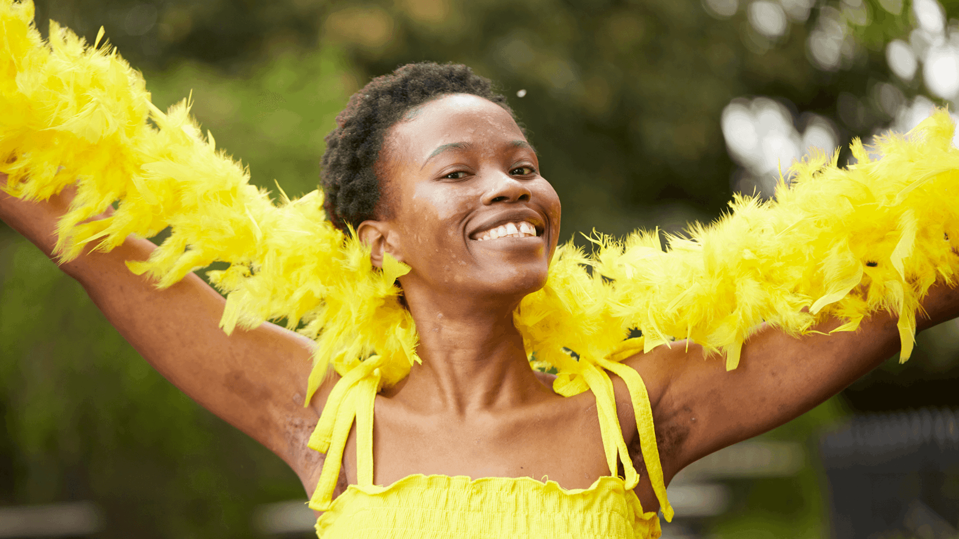 medium shot of a fundraising ambassador wearing yellow dress and yellow feather scarf smiling at the camera