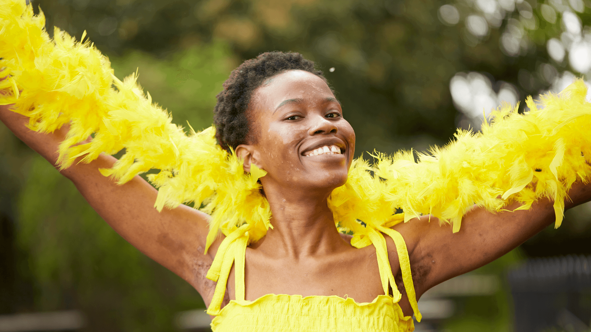 medium shot of a fundraising ambassador wearing yellow dress and yellow feather scarf smiling at the camera