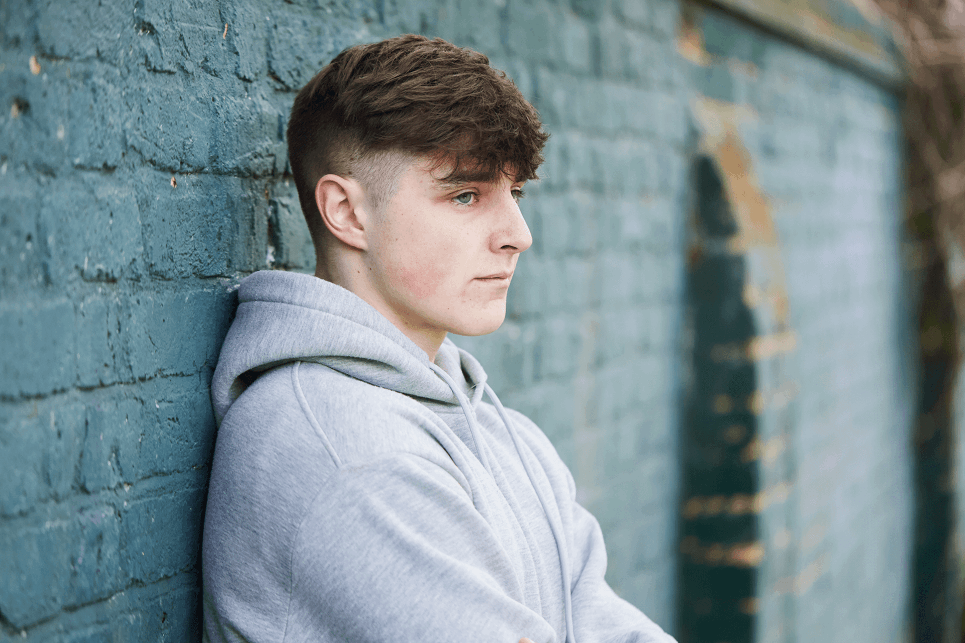 A young person standing with their back against a brick wall.