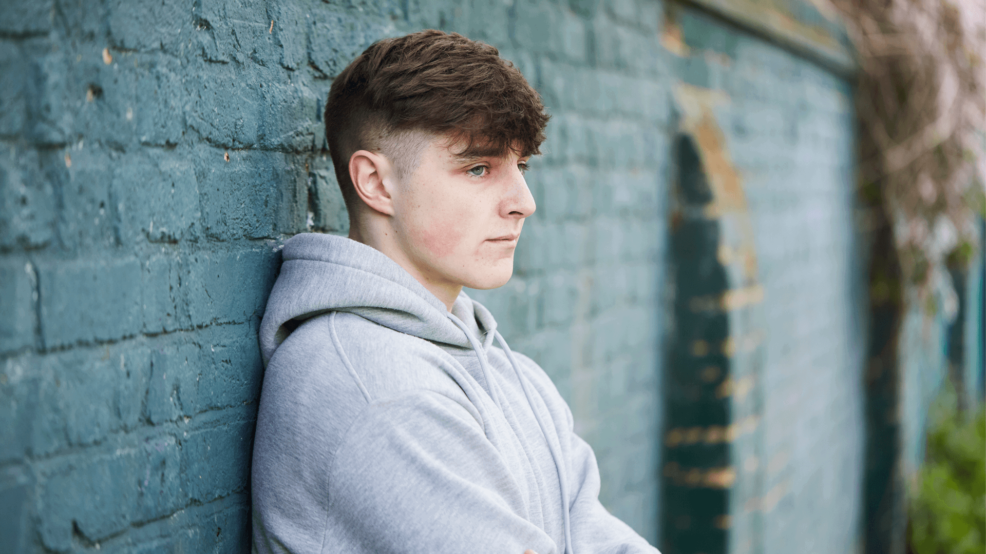 A young person standing with their back against a brick wall.