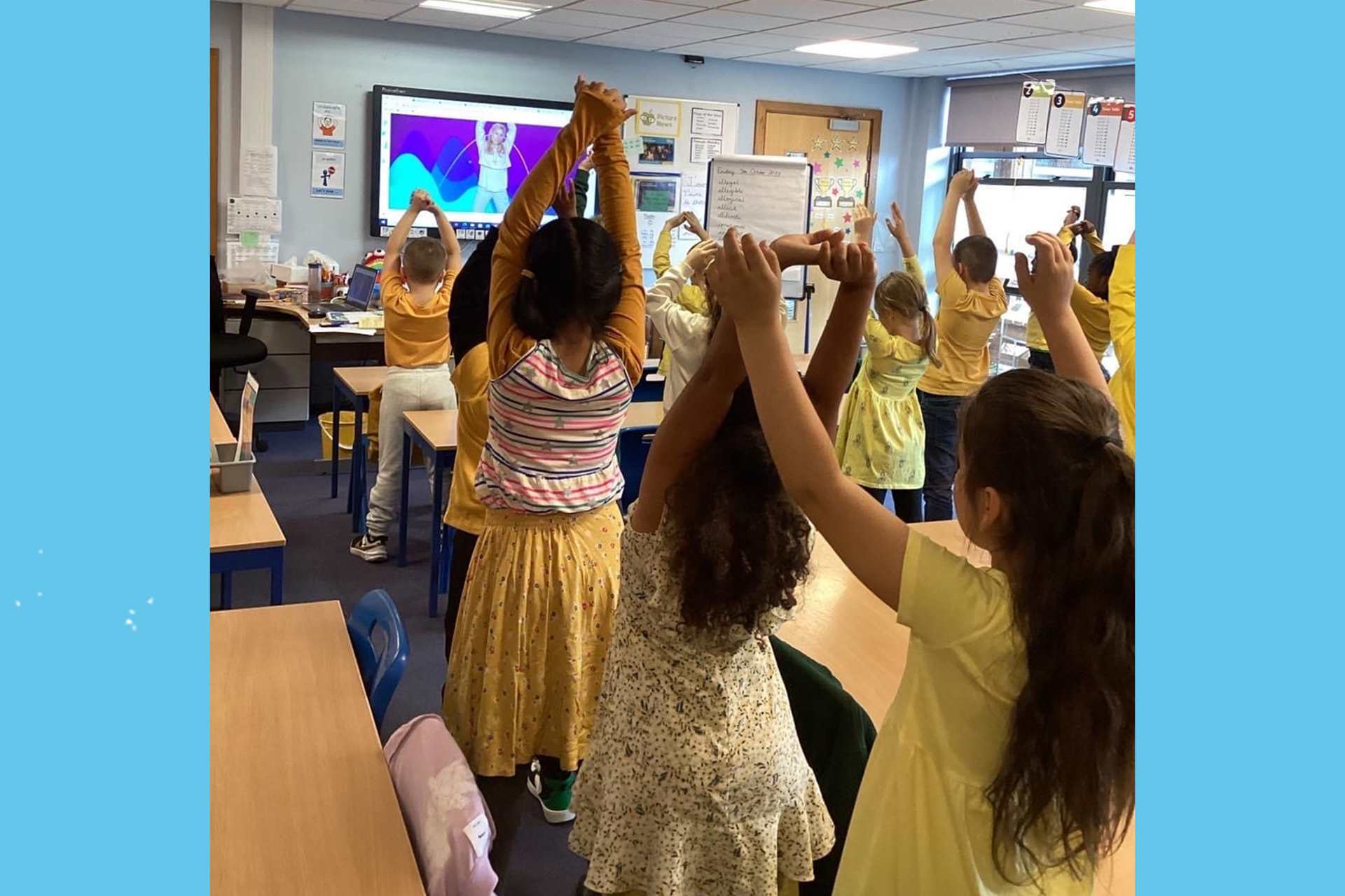 A primary school class all dressed in yellow with their hands in the air.