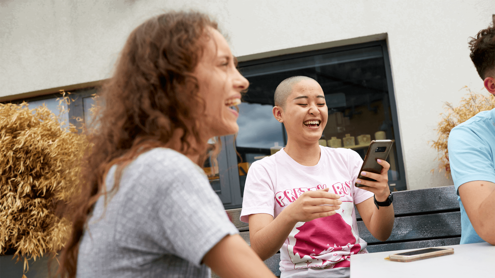 two-young-woman-laughing-while-one-is-hlding-her-phone-and-another-one-is-looking-at-their-friends-cropped-in-photo