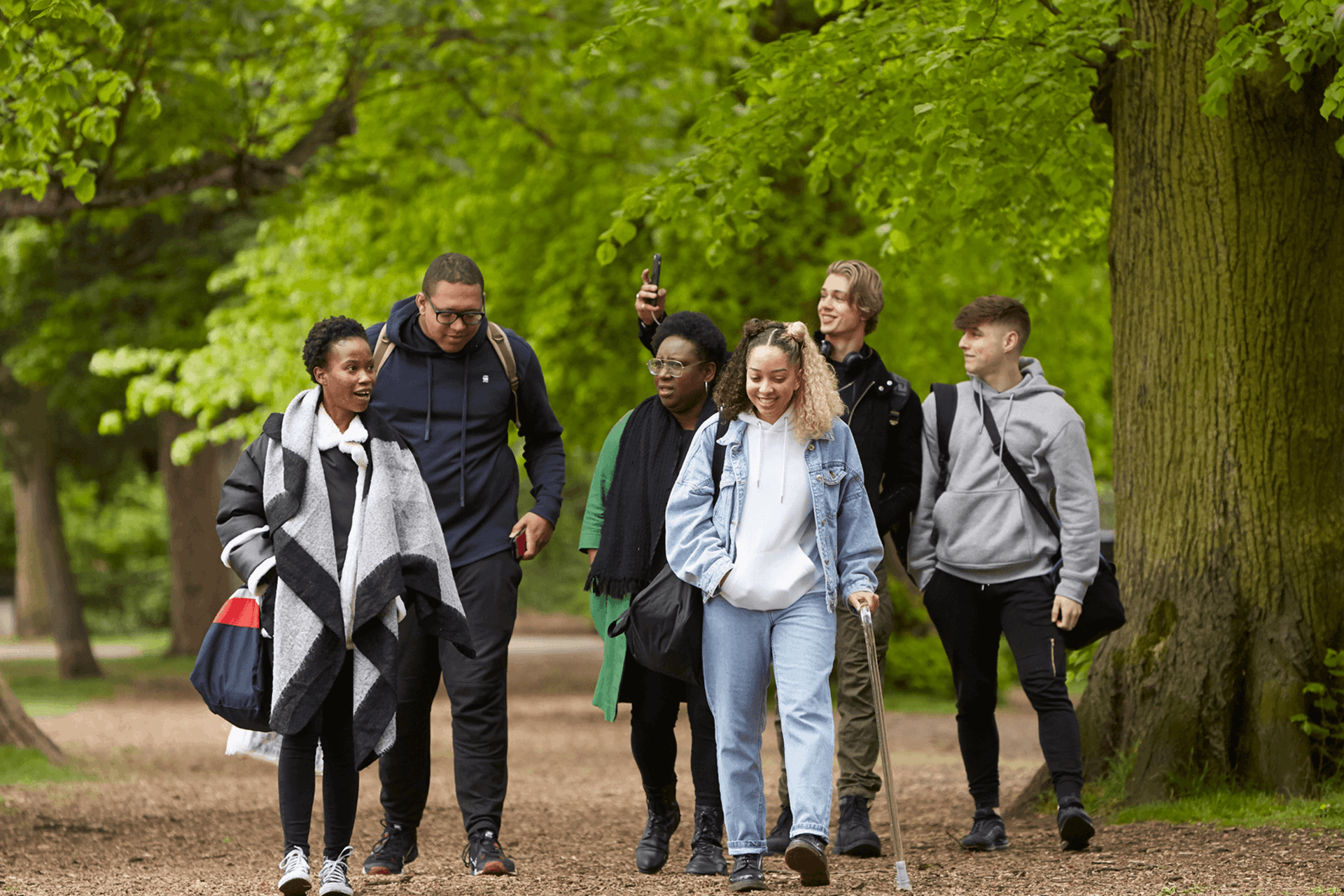 A group of six young people talking and smiling together while walking through the woods.