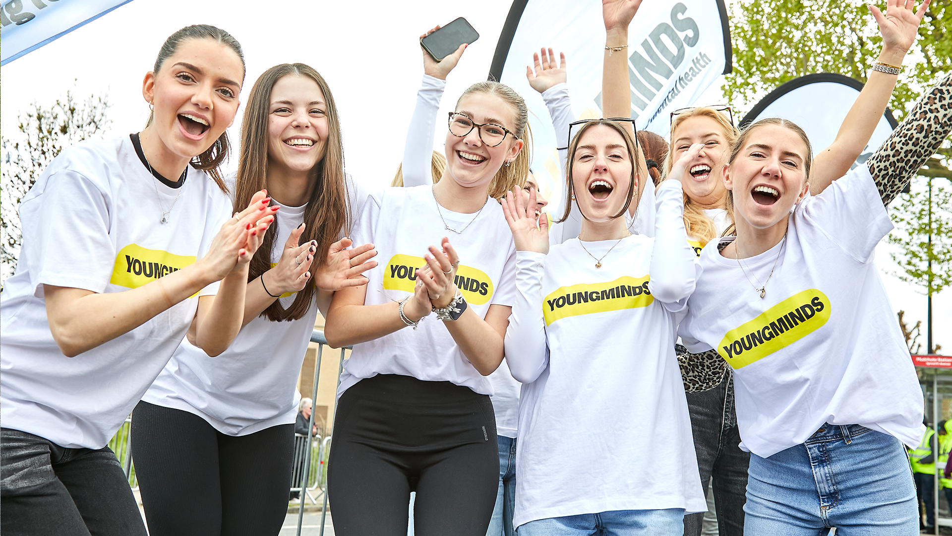 The YoungMinds fundraising team cheering with their hands in the air at the marathon. They are wearing YoungMinds t-shirts and have YoungMinds banners.