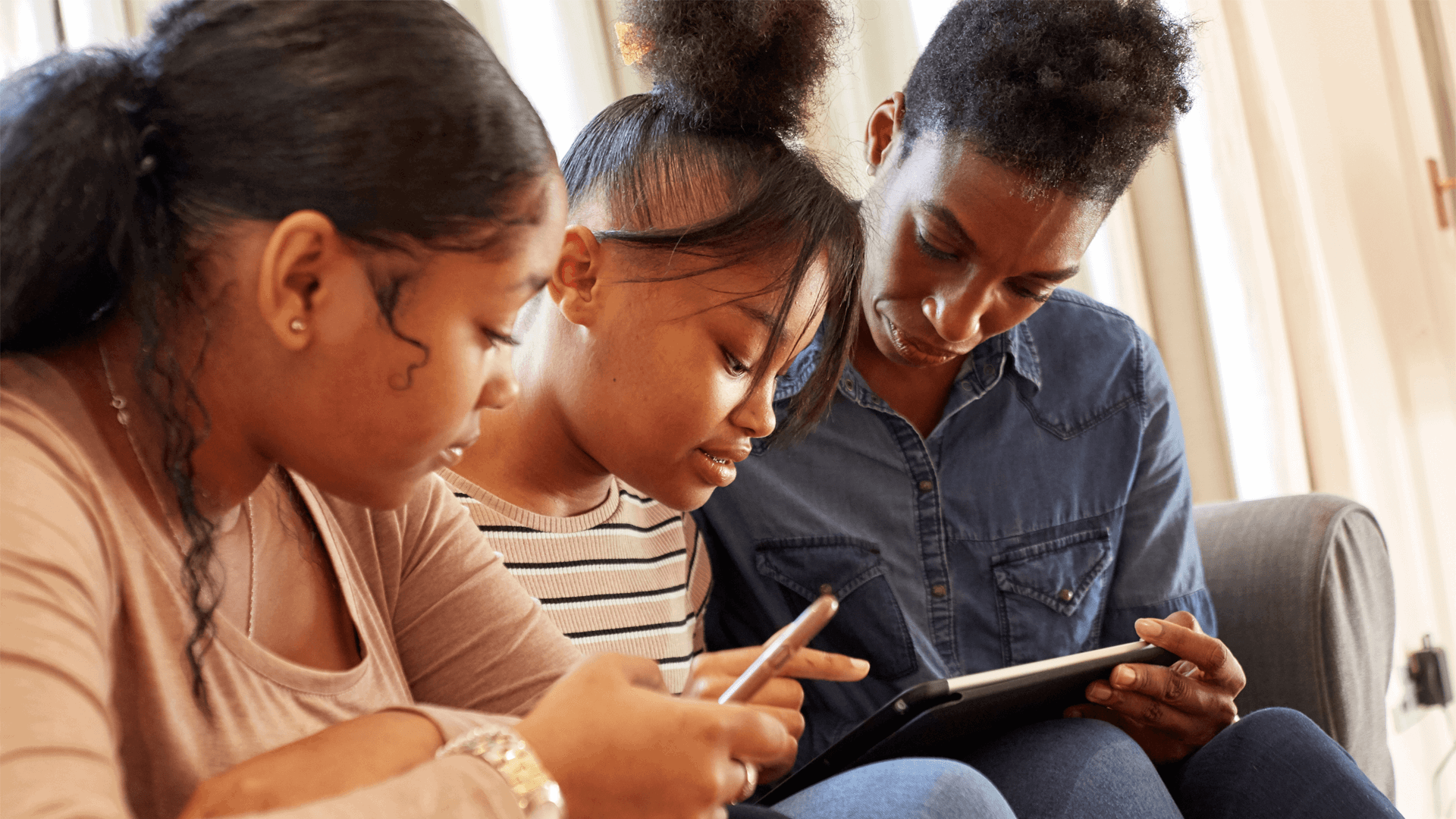 A mother and her daughters sitting together using a mobile phone and tablet 