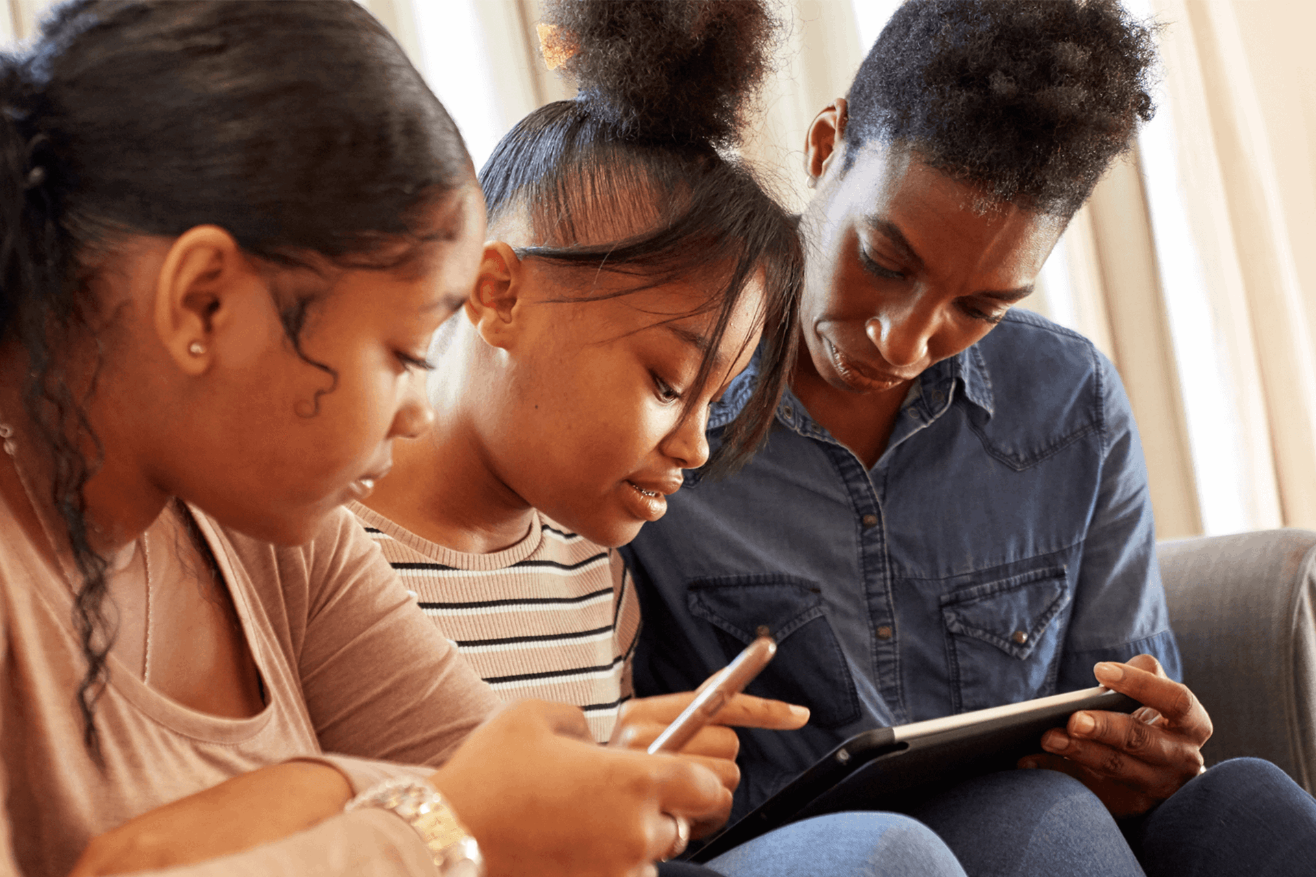 A mother and her daughters sitting together using a mobile phone and tablet