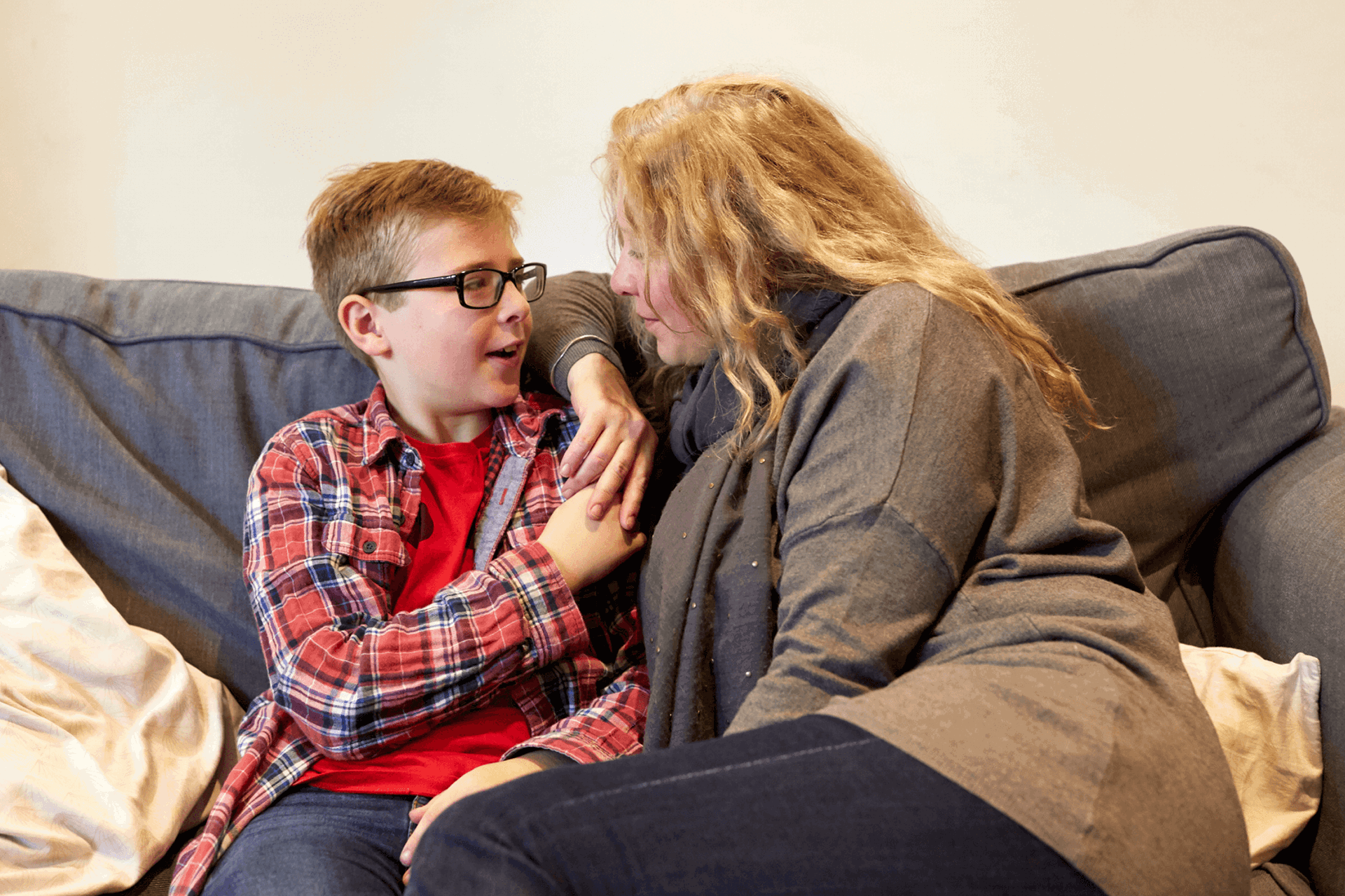 A mother and her young son hold hands on the sofa