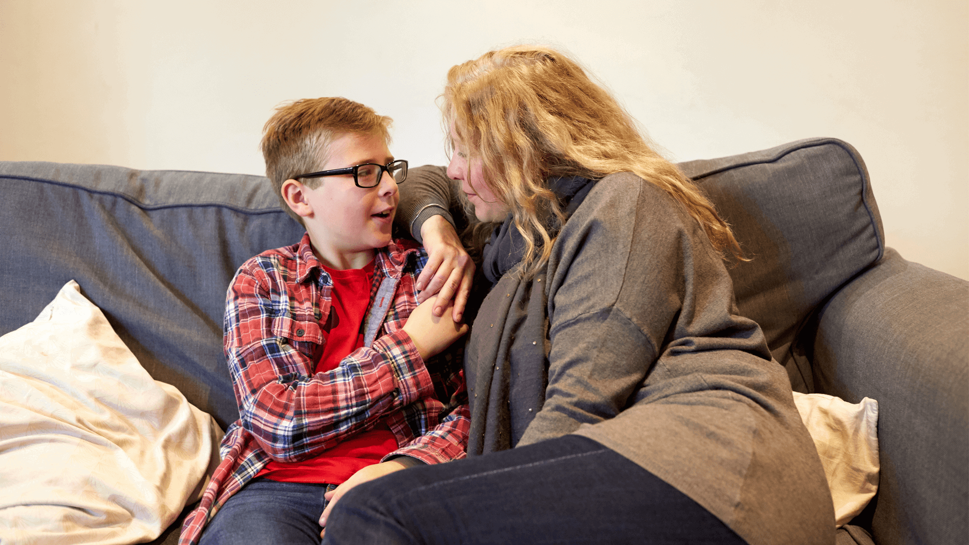 A mother and her young son hold hands on the sofa