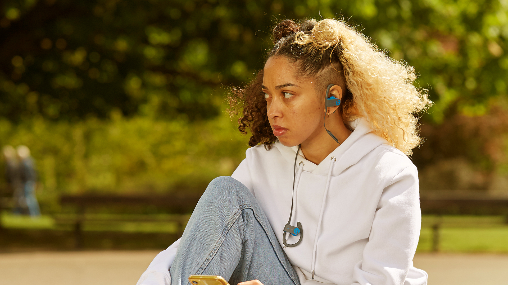 A girl listening to music in the park looking worried.