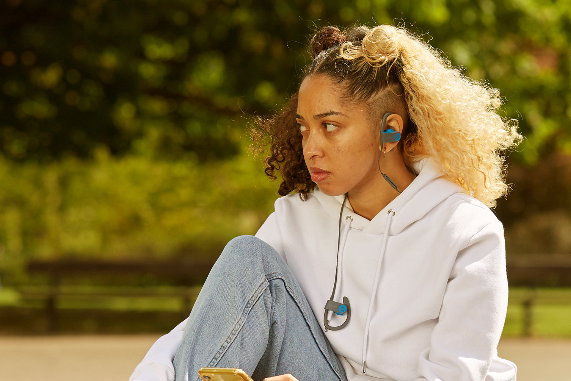 A girl listening to music in the park looking worried.