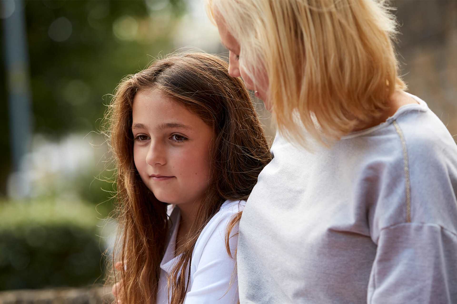 A mother comforts her sad looking daughter outdoors