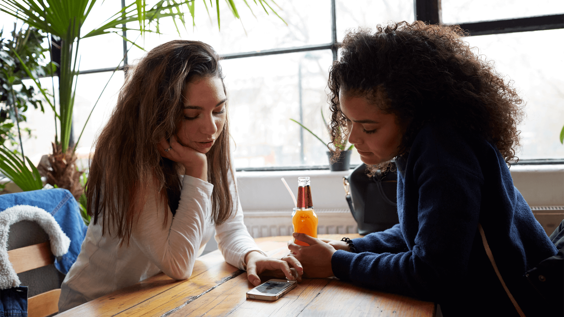 two-young-woman-sitting-inside-a-restaurant-looking-at-a-phone-on-the-table