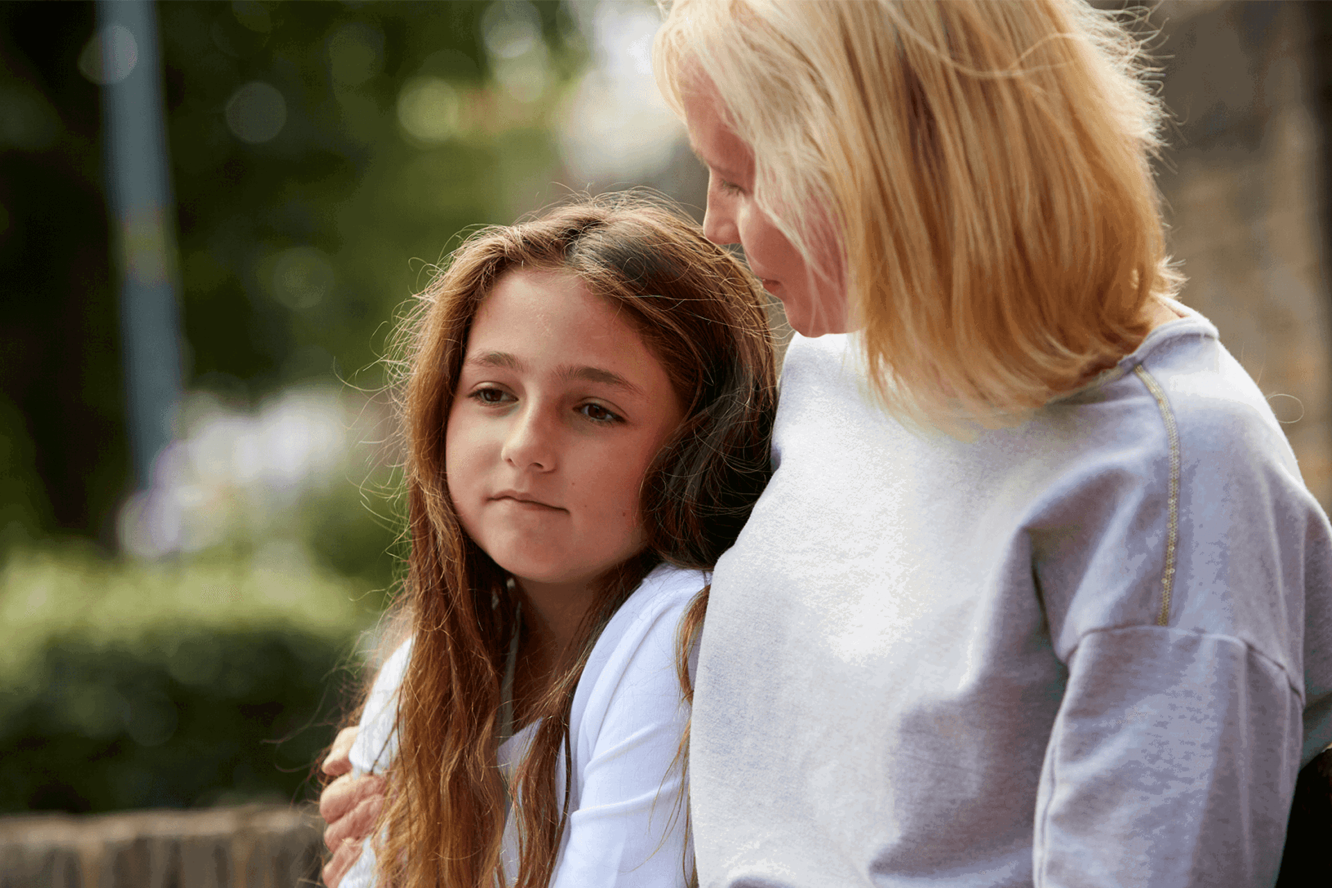 A lady comforts a young girl outside by sitting putting her arm around her