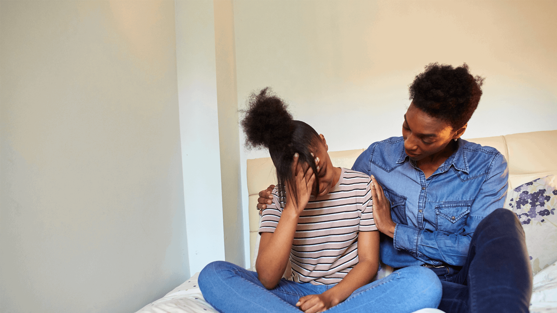A mother comforts her upset daughter on a bed