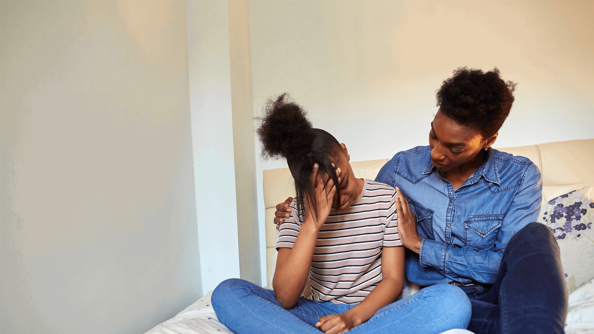 A mother comforts her upset daughter on a bed 