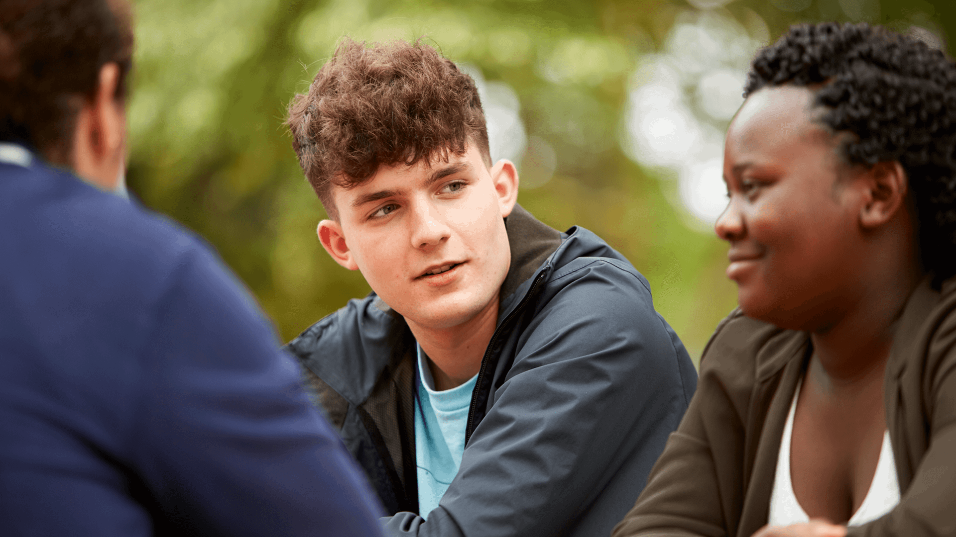 Close up of three young people talking and smiling while in the park.