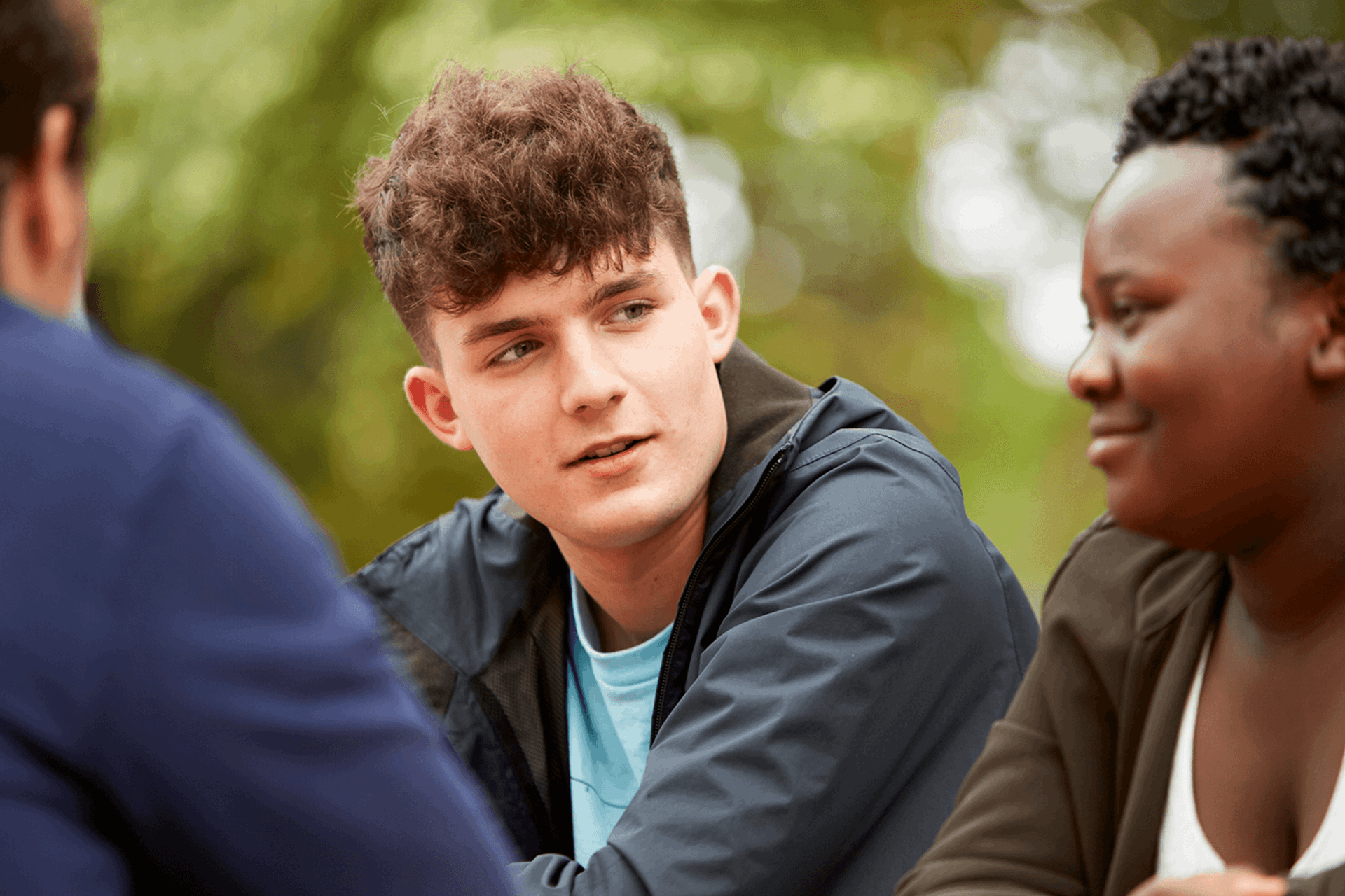 Close up of three young people talking and smiling while in the park.