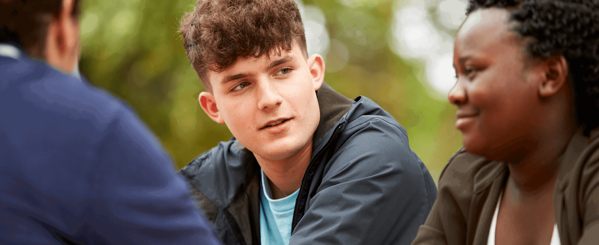 Close up of three young people talking and smiling while in the park.