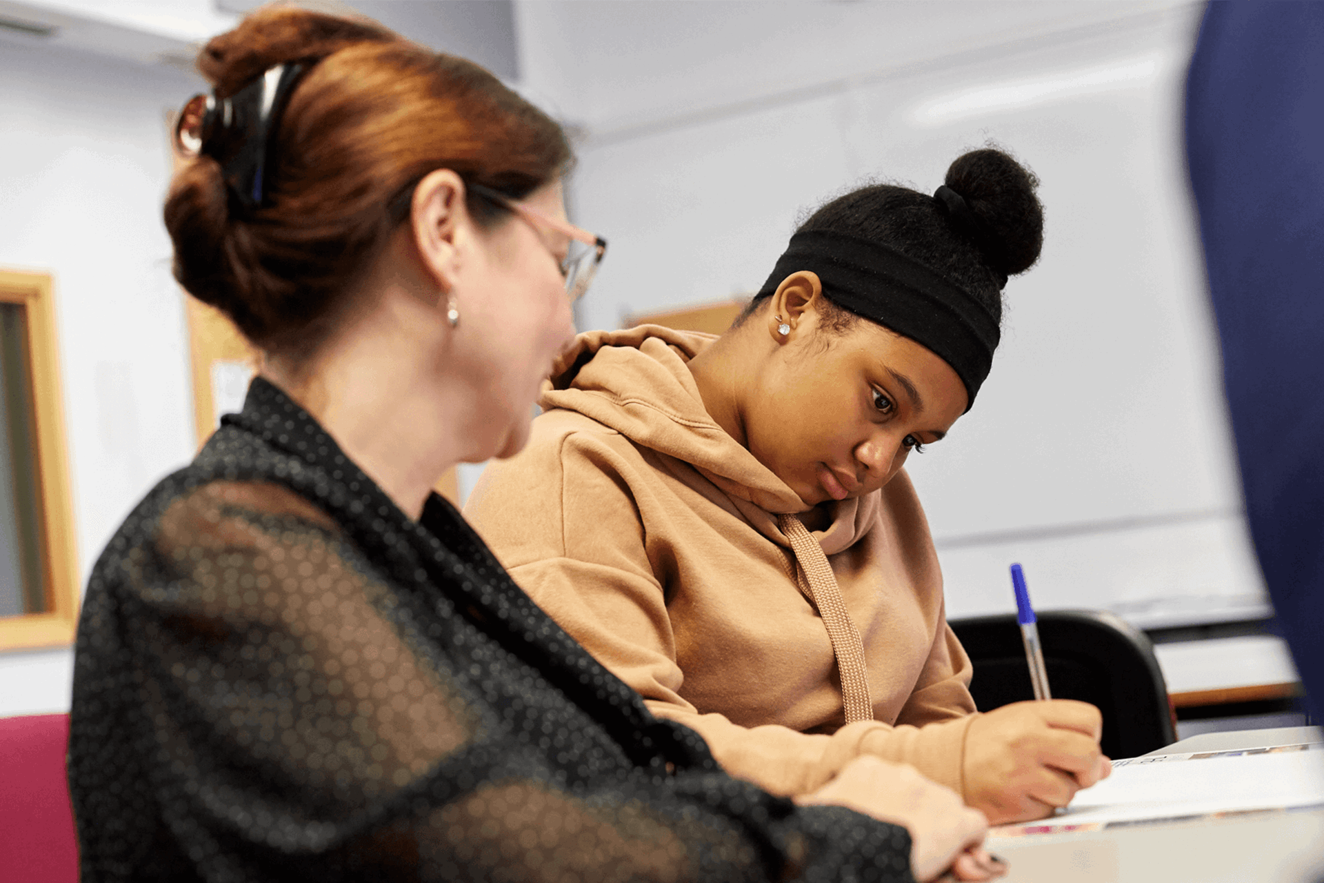 a teacher sits beside a student to help her as she answer her exam