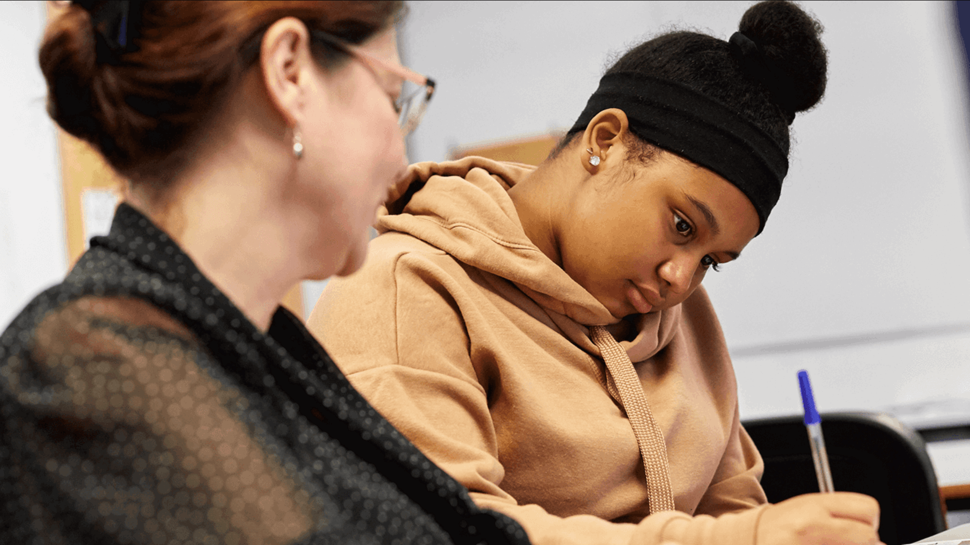 a teacher sits beside a student to help her as she answer her exam