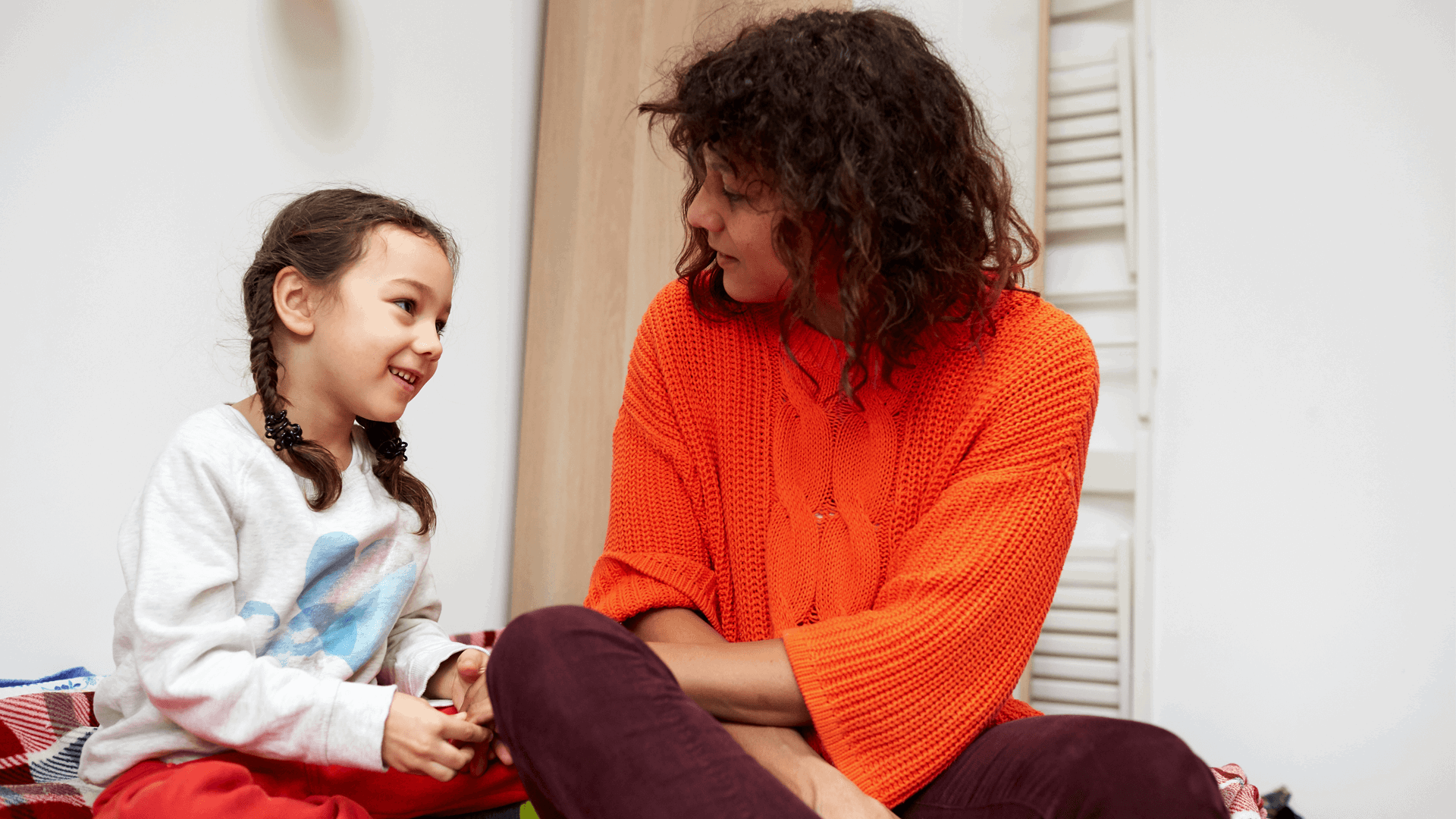 A mother and daughter sit and talk on the bed together