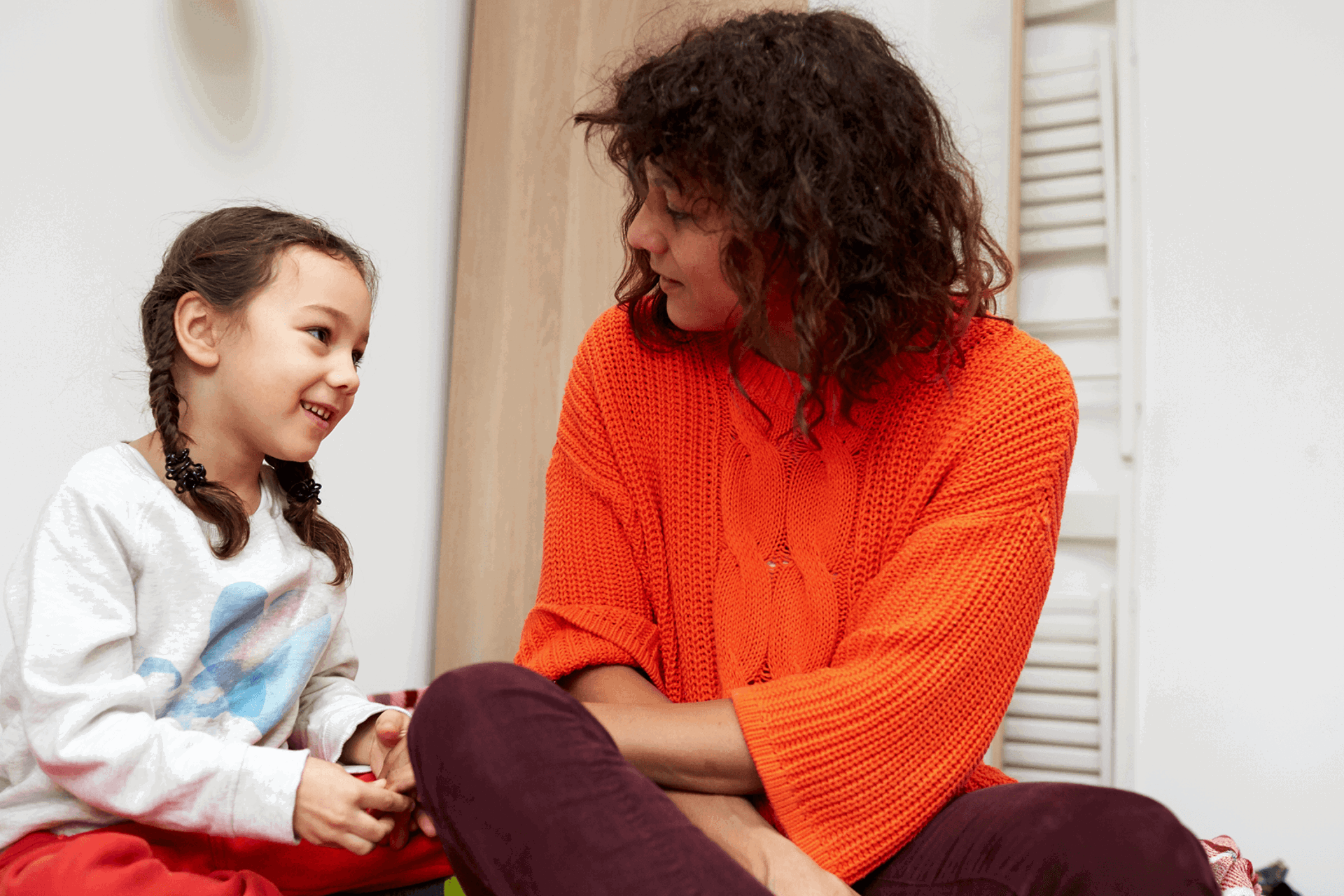 A mother and daughter sit and talk on the bed together