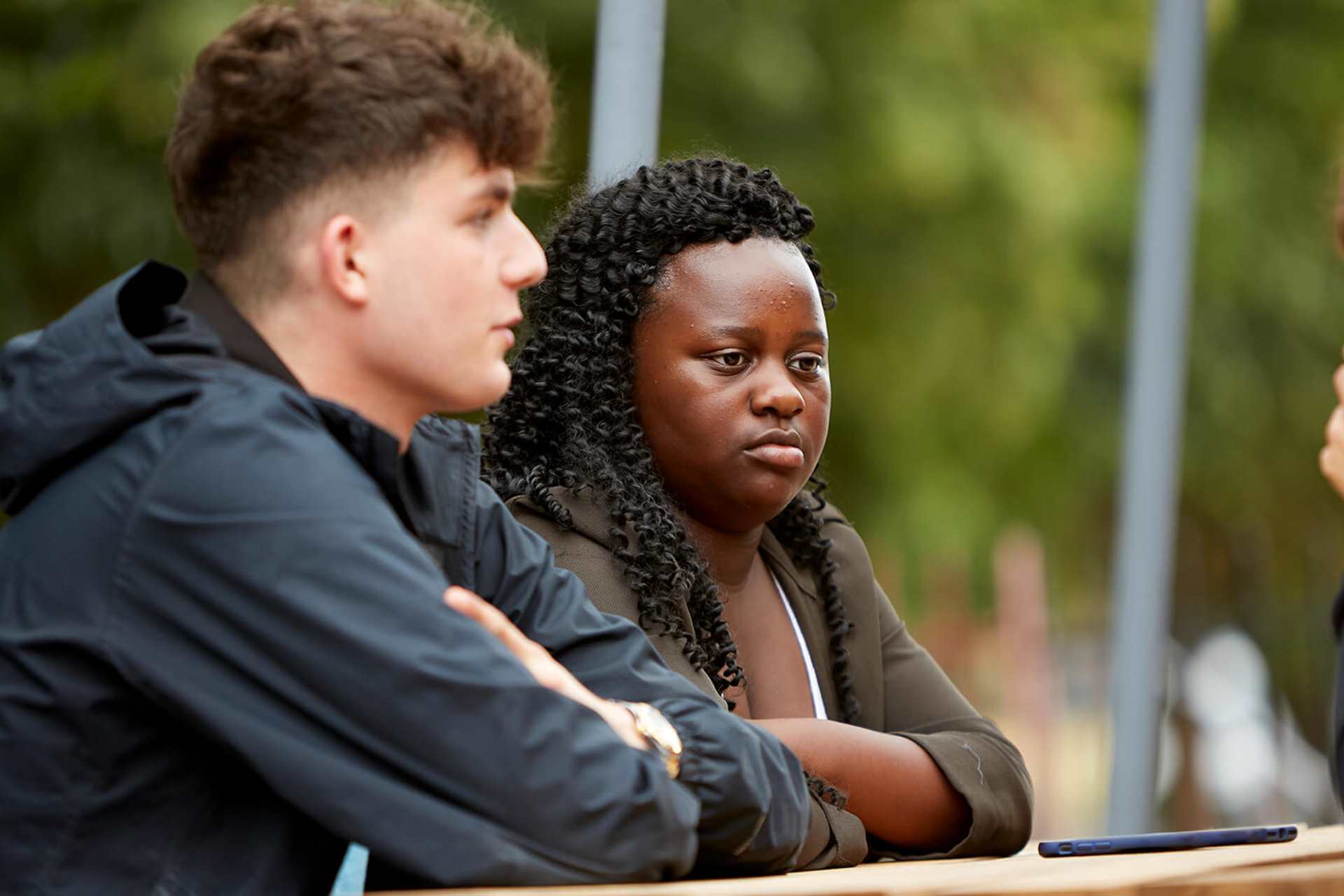 Two young people listening intently to their friend while sitting on a bench in a park.
