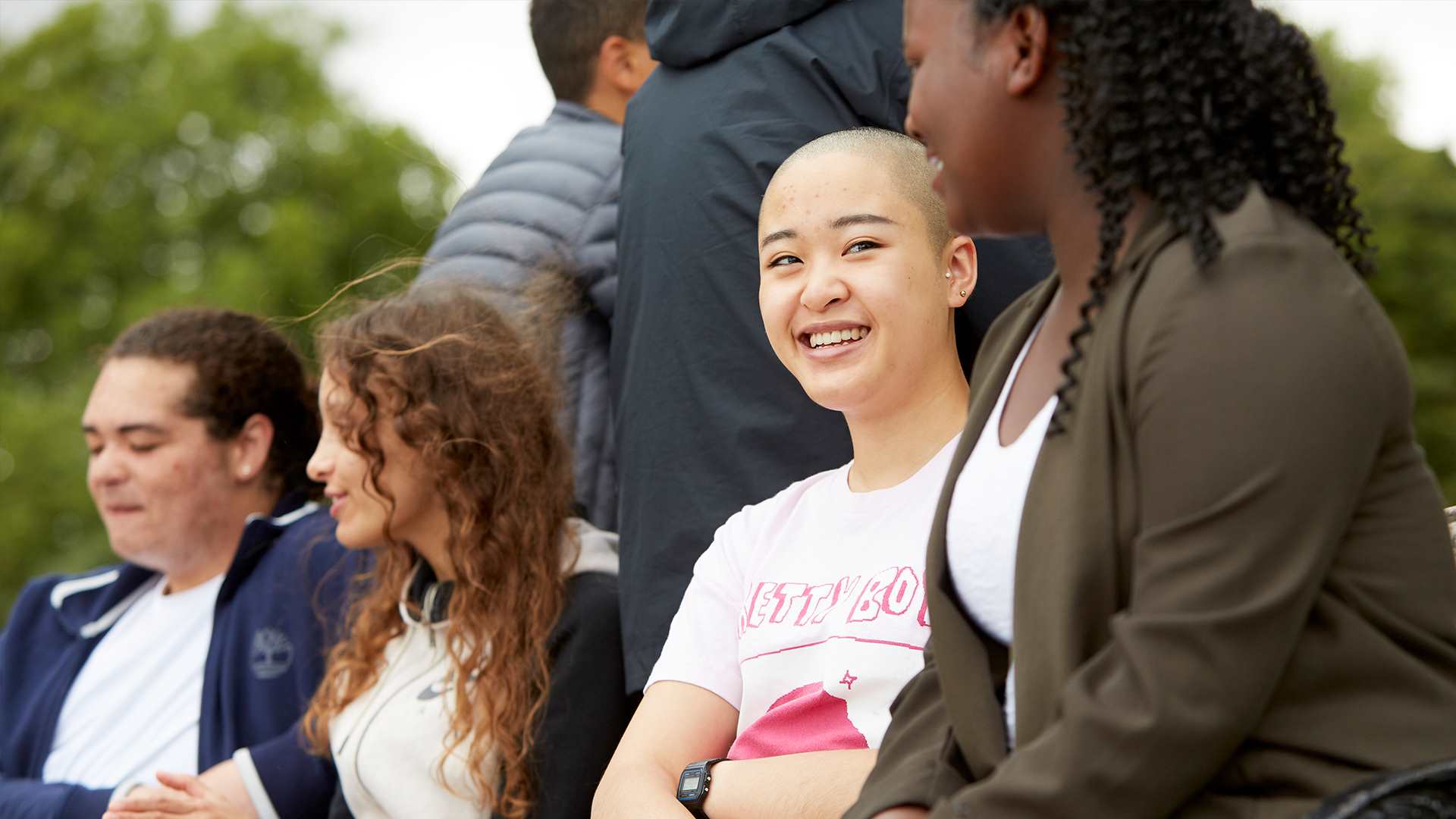 A group of young people sitting in a park talking and smiling at each other.