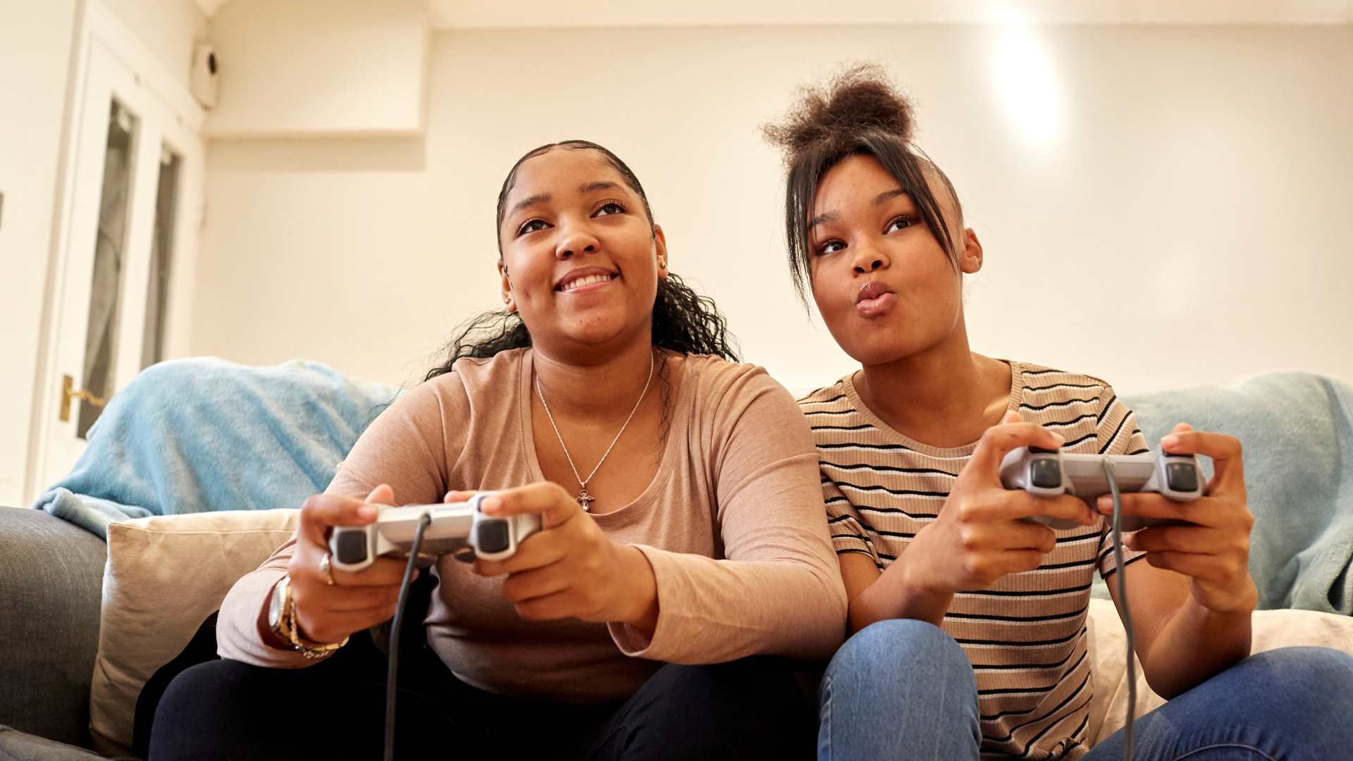 Two young people playing PlayStation on the sofa.